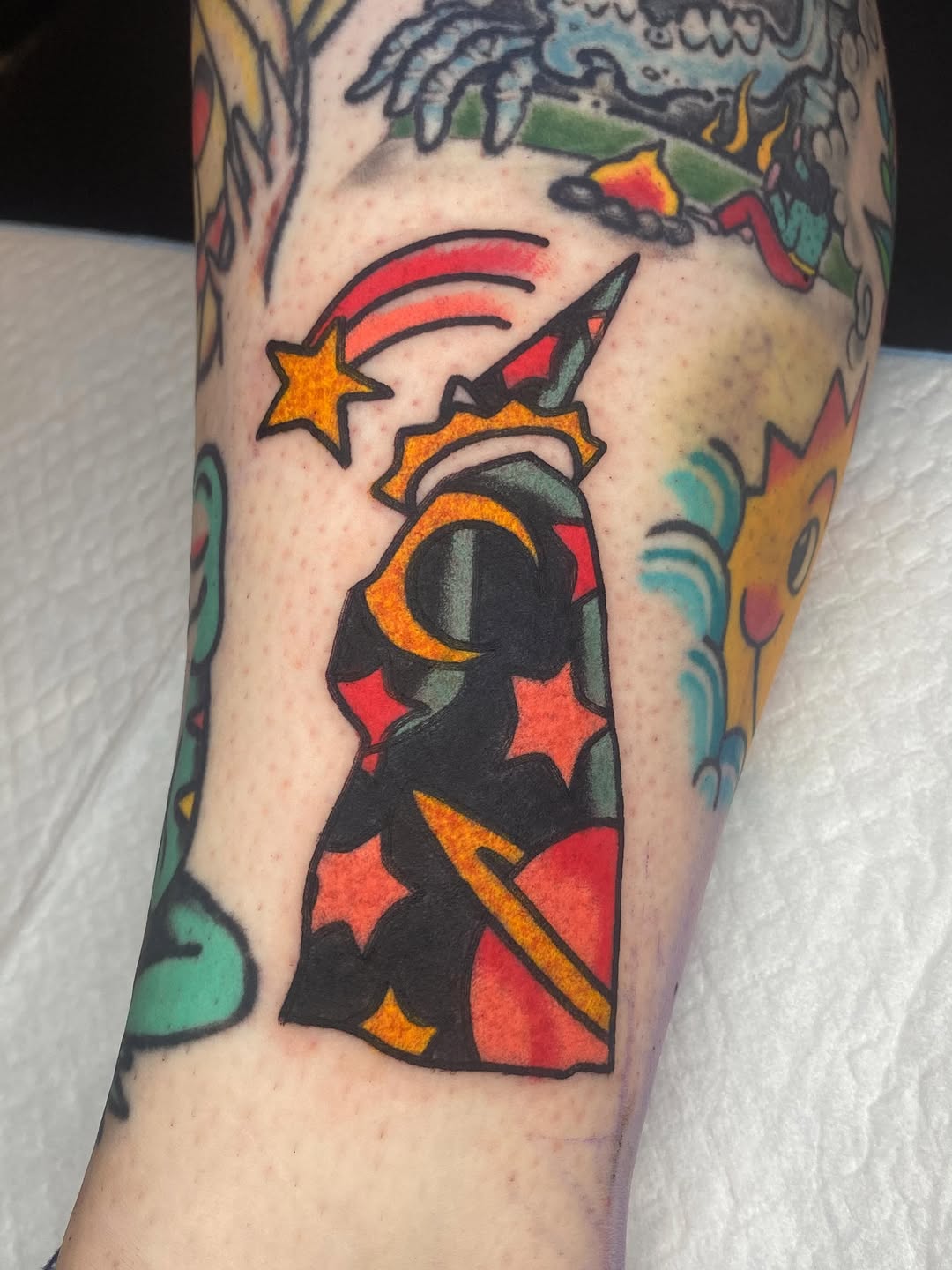 Dynamite stick with lit fuse, red and orange stars, crescent moon, and shooting star on forearm.