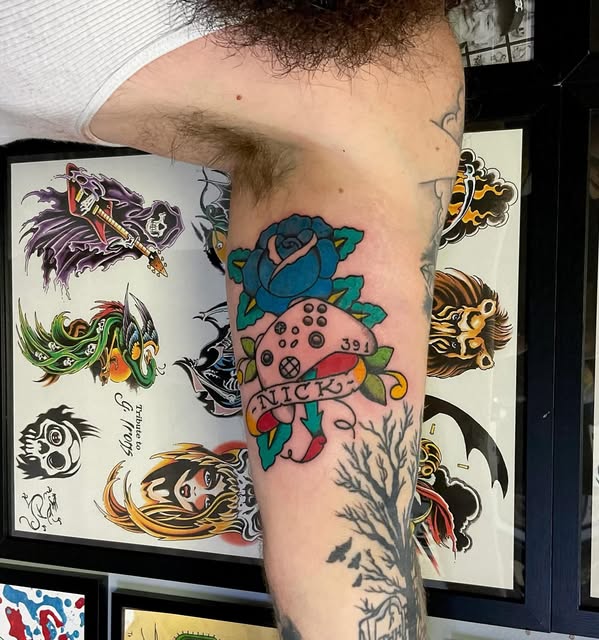 Strawberry Shortcake character tattoo on upper arm featuring a pink strawberry with blue-green leaves and the name 'NICKY' on a person's shoulder.