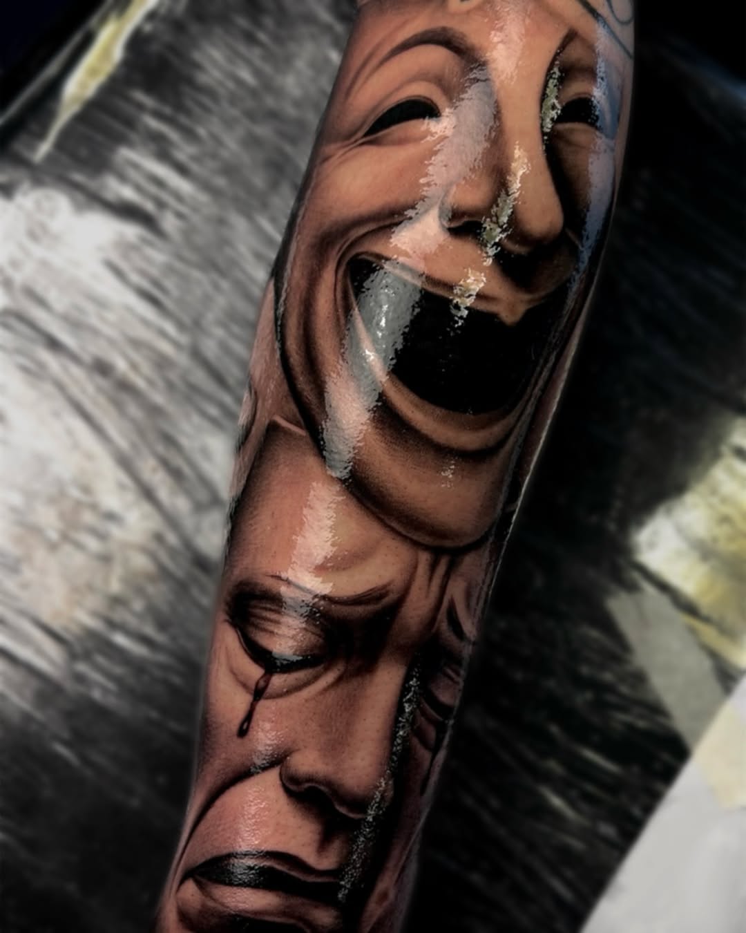 Two realistic male faces with detailed shading and emotional expressions tattooed on the forearm in black and grey ink.