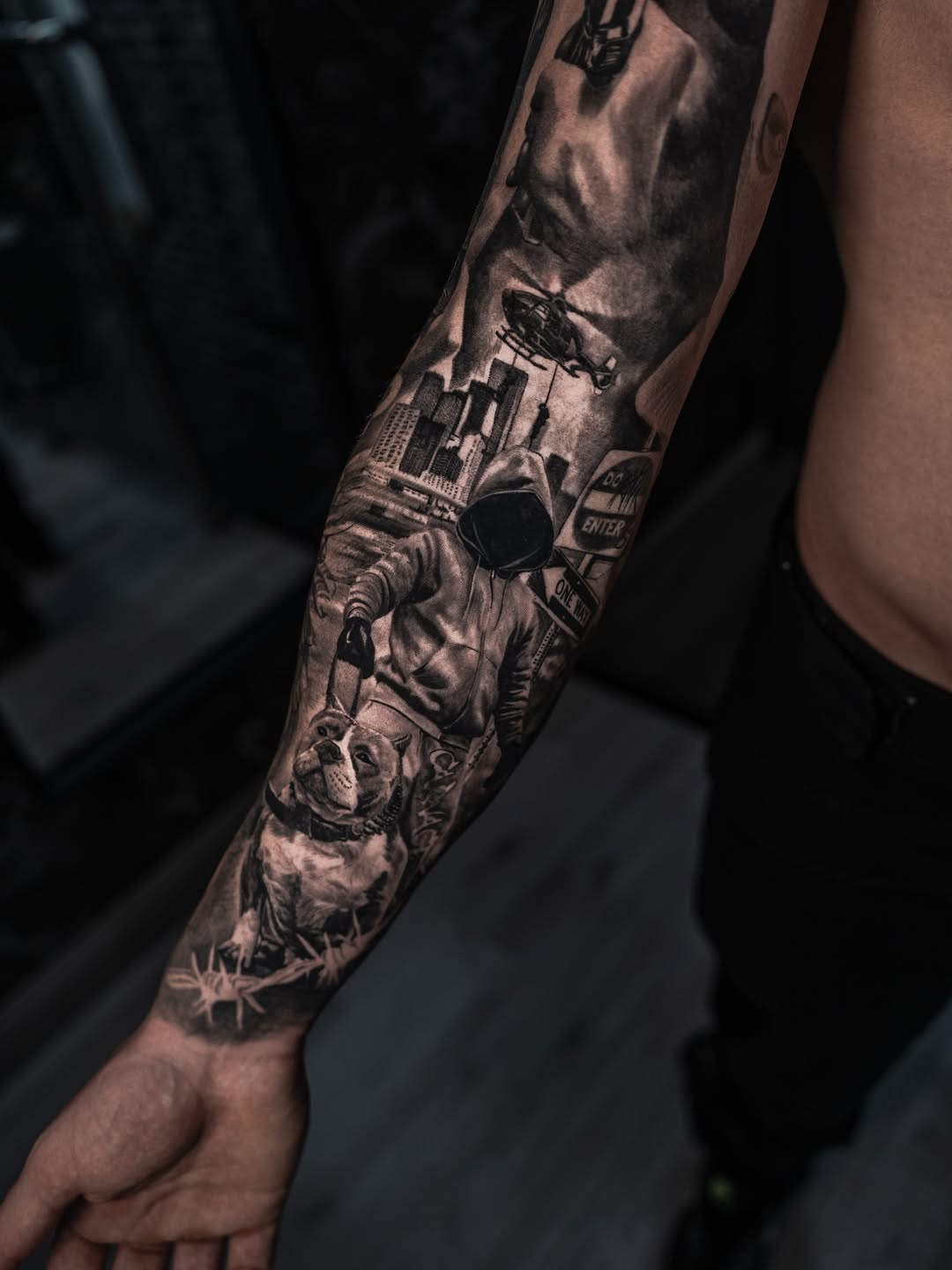 Full-sleeve monochrome realistic tattoo featuring astronaut, city skyline, helicopter, and skull imagery on forearm.