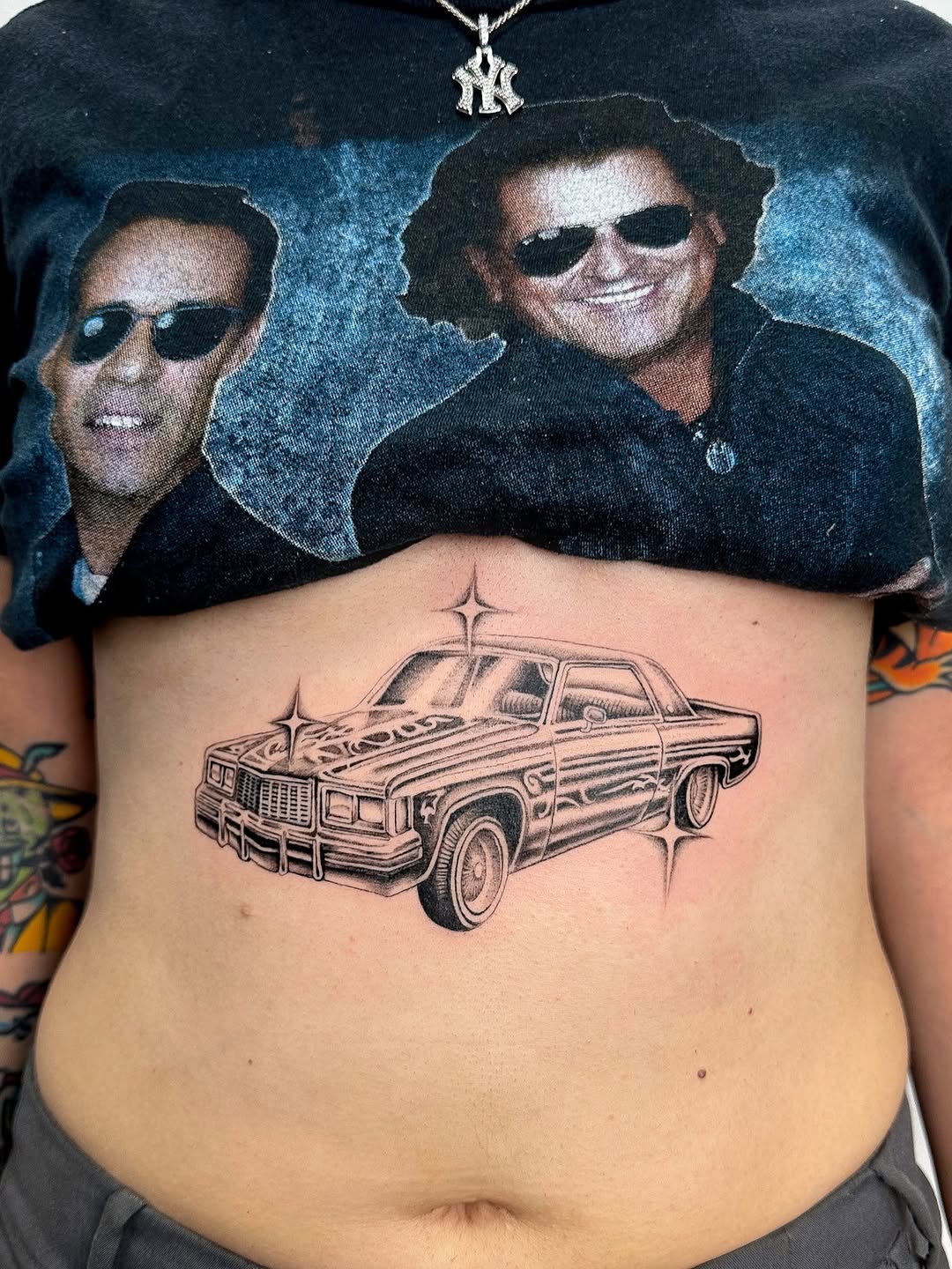 Black and grey lowrider car tattoo on chest with four-pointed star crosses, detailed shading and chrome details.