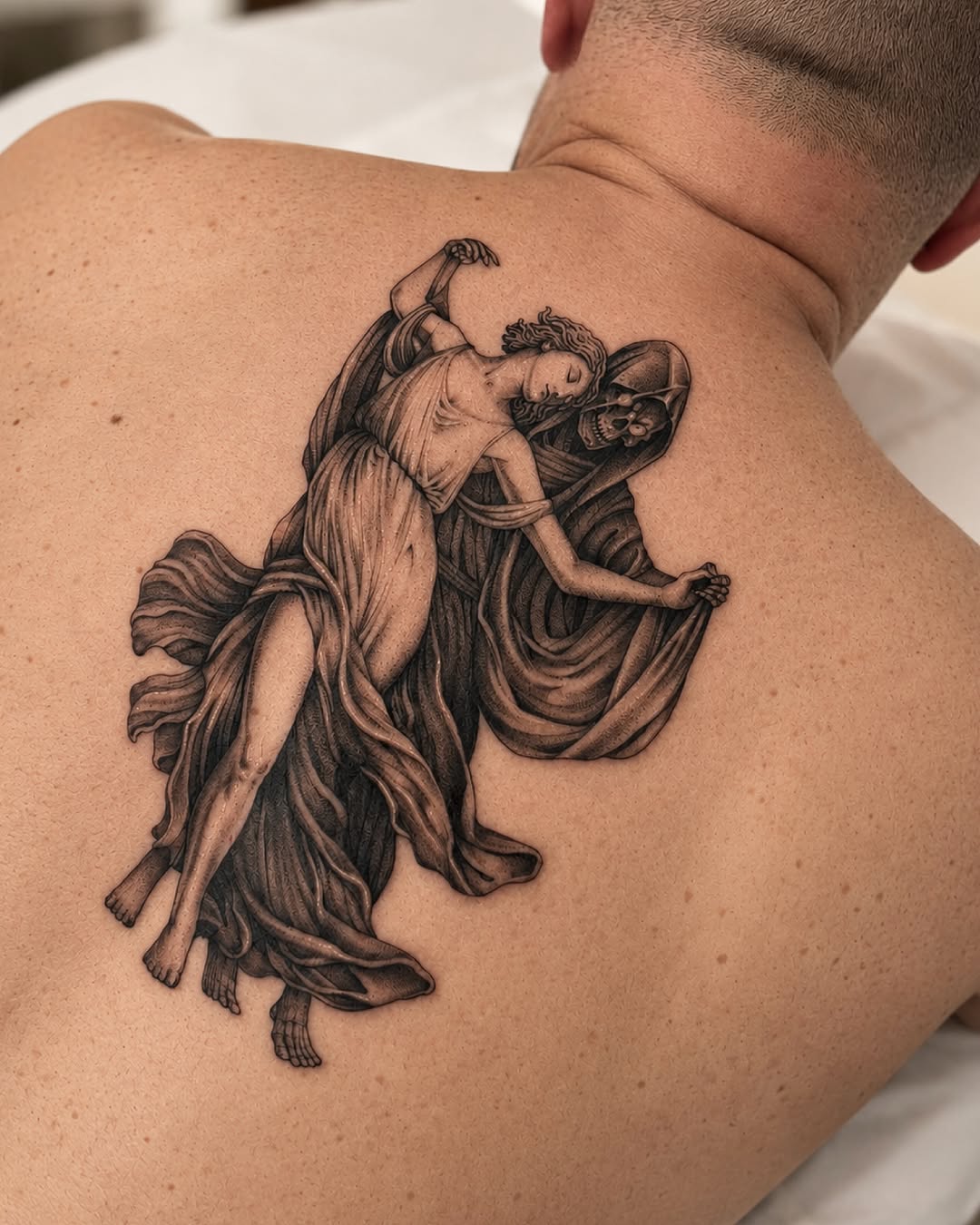 Classical winged female figure in flowing robes with detailed shading on upper back, rendered in black and grey ink.