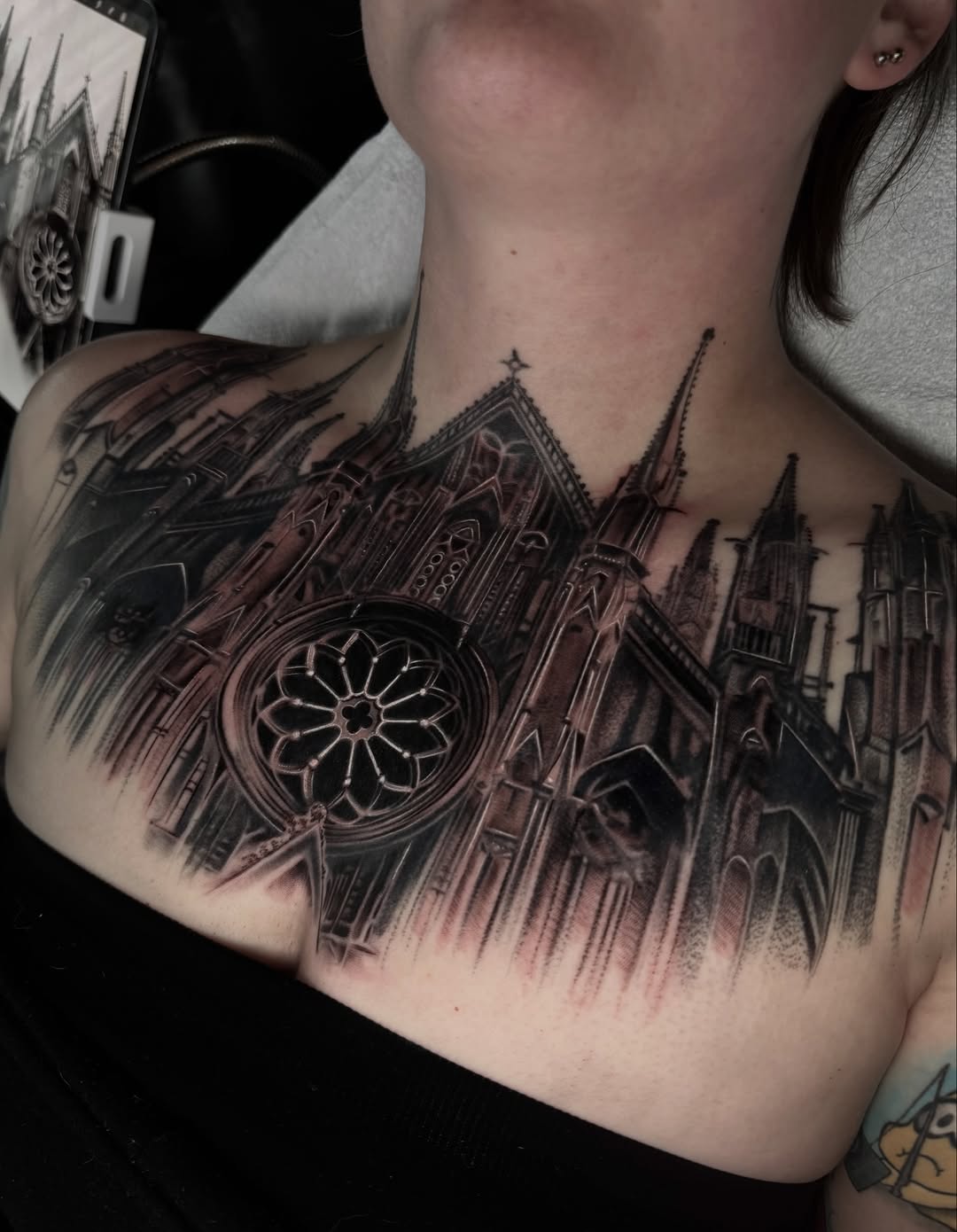 Detailed Gothic cathedral tattoo on shoulder and chest featuring ornate rose window and spires in black and grey tones.
