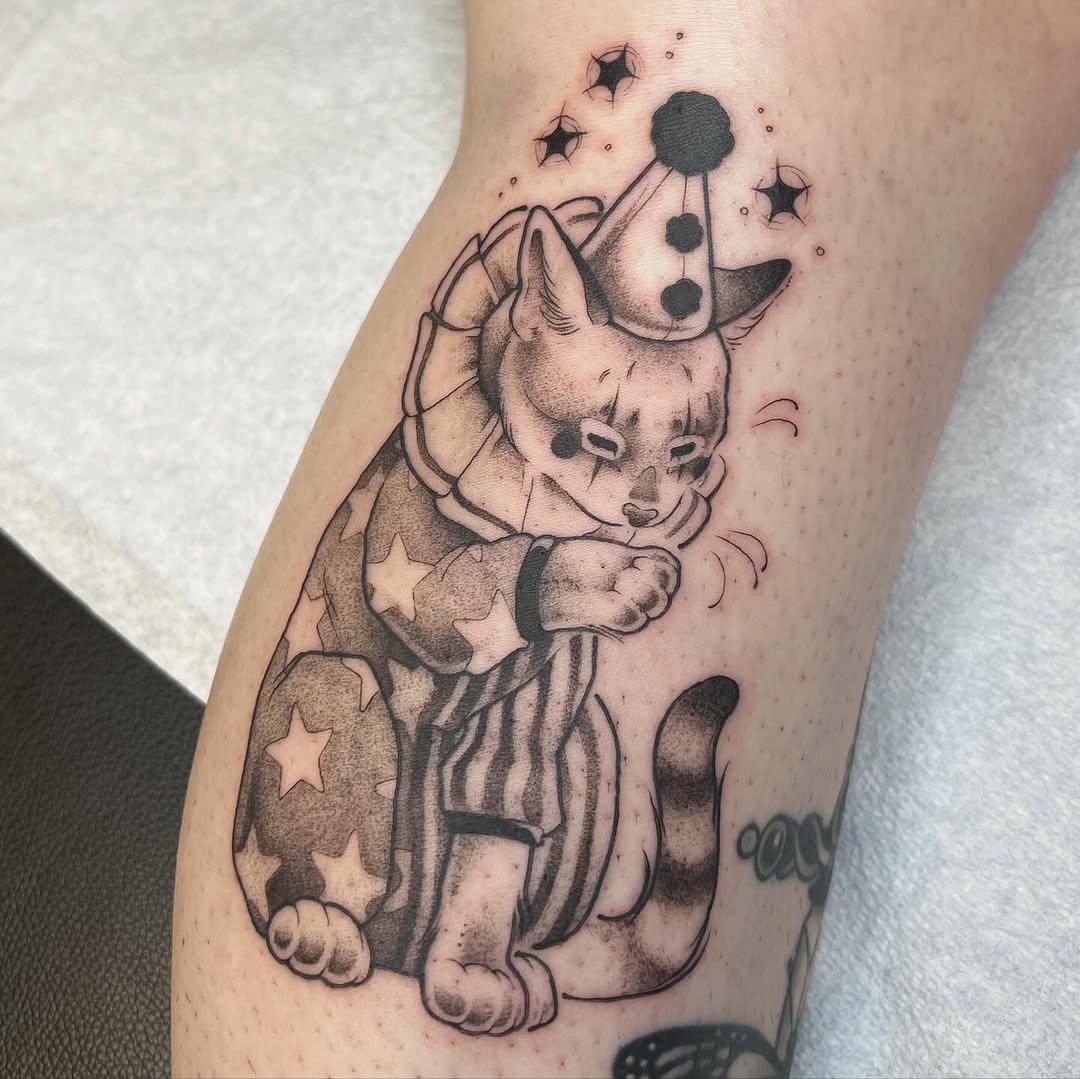 A whimsical dog wearing a party hat with dangling celestial ornaments on its head, adorned with stars and planets on its body, rendered in black and grey shading on the leg.
