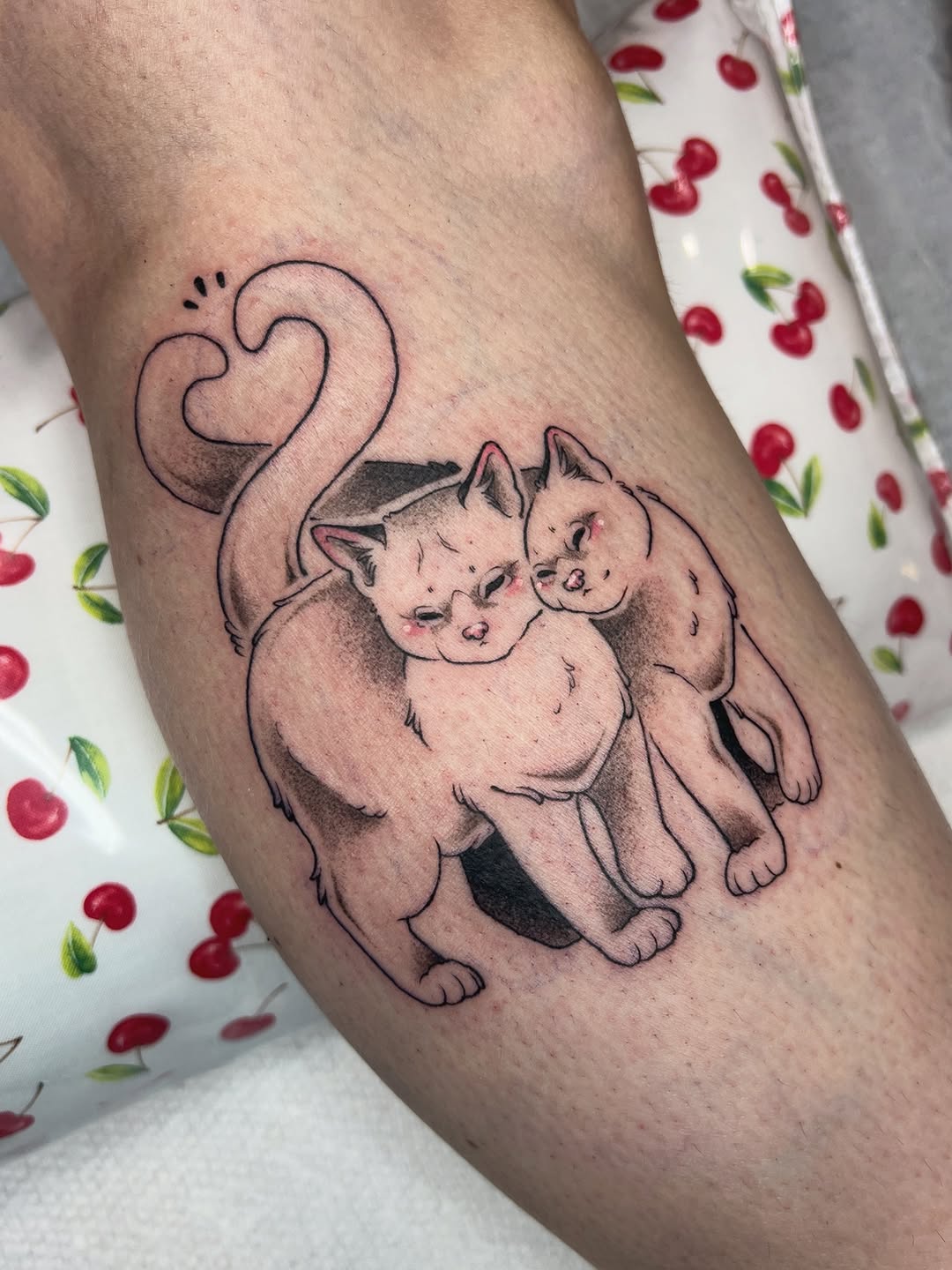 Mother cat with two kittens and curled tail on upper arm, rendered in black and grey with soft shading.