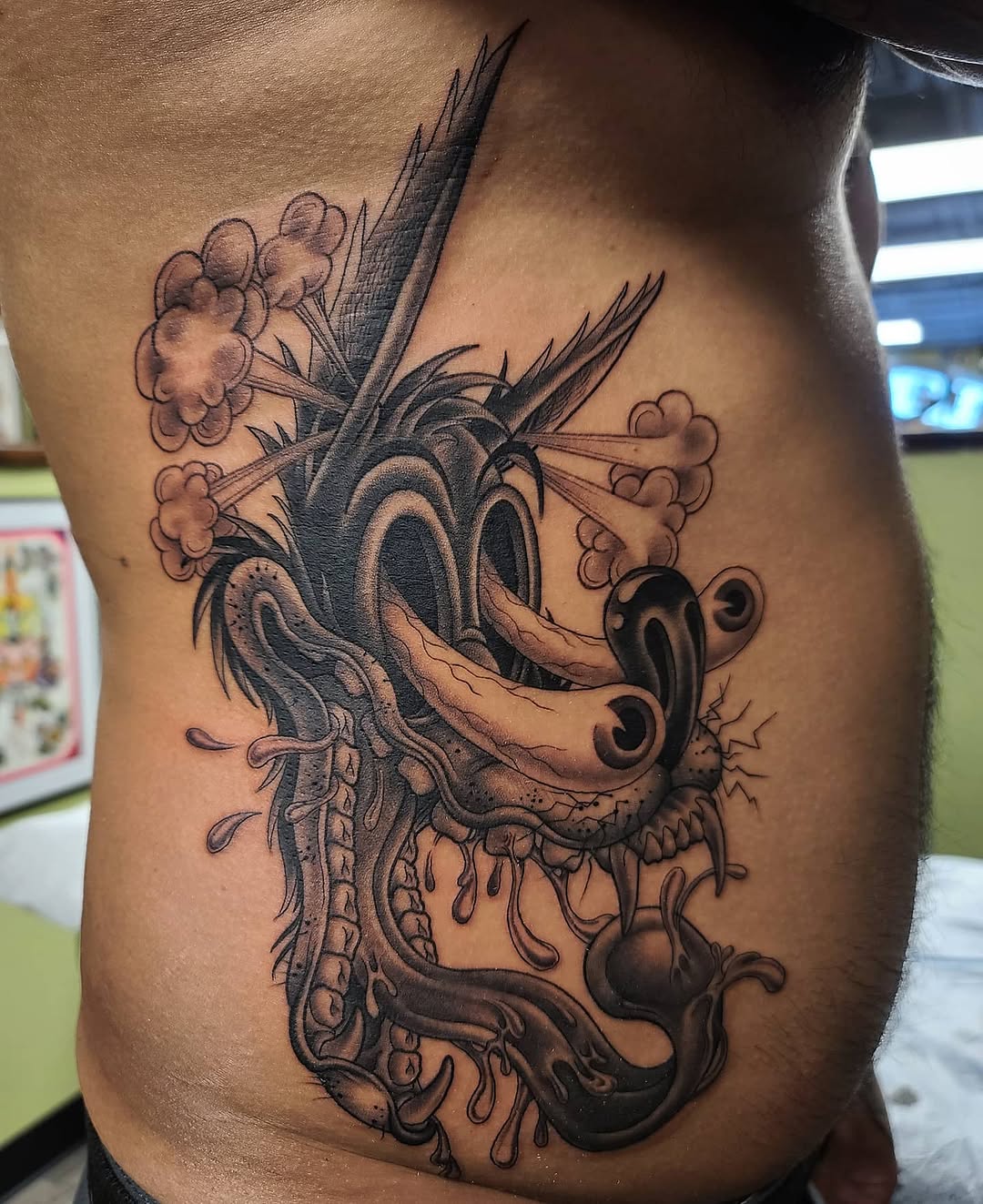 Dragon head tattoo with ornate details and flowing tendrils on torso, rendered in black and grey with soft shading.