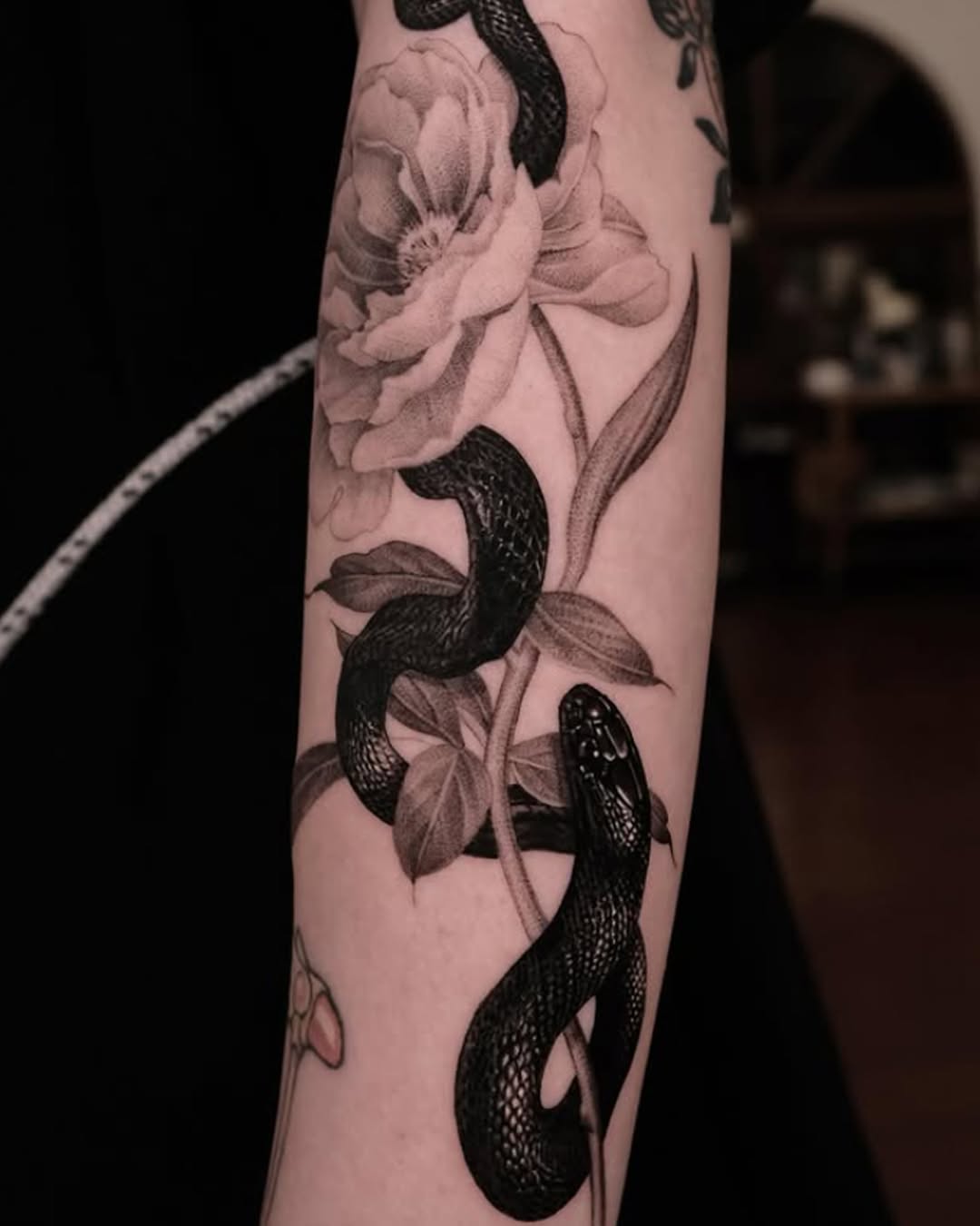 Black and grey tattoo of snakes intertwined with detailed flowers on an arm, featuring realistic shading and botanical elements.