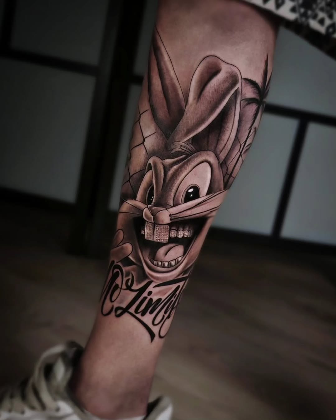 Cartoon rabbit character with large ears and wide grin wearing a bow tie, tattooed on calf with script text below in black and grey.