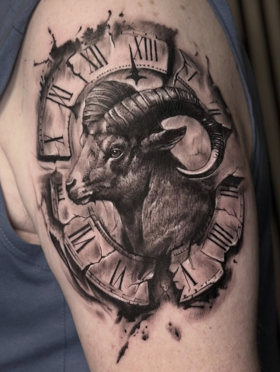Ram's head with curved horns in profile, surrounded by Roman numeral clock faces with watercolor splatter effects, rendered in black and grey on upper arm.