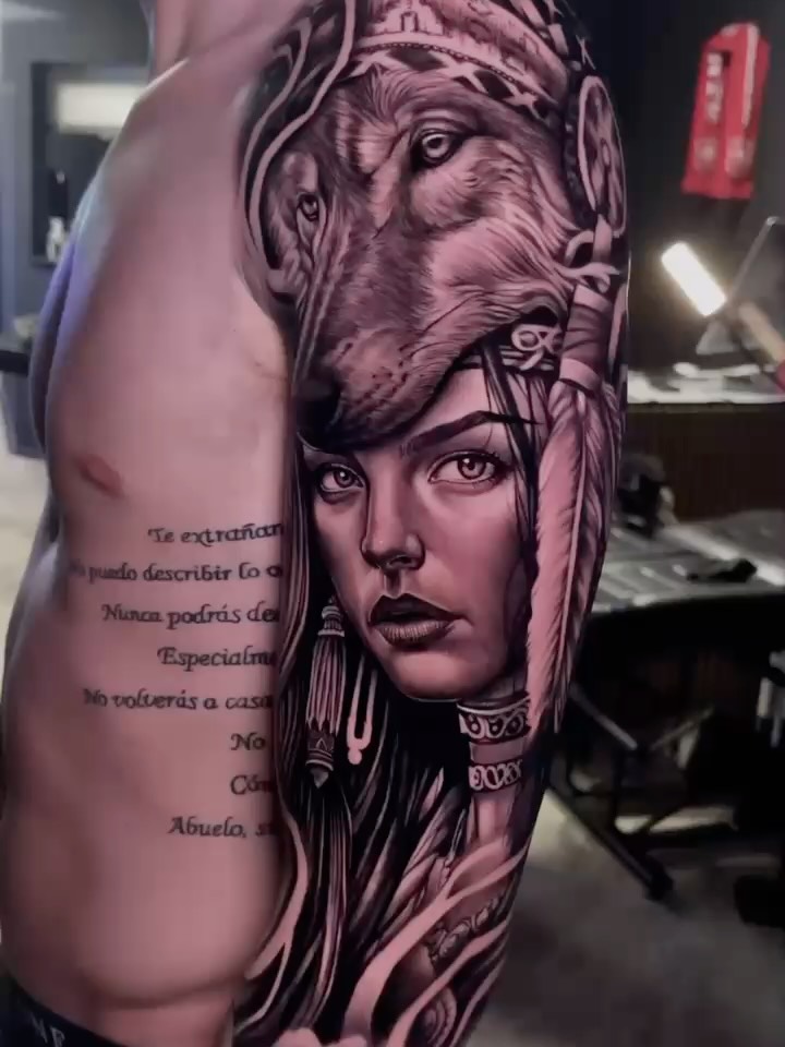 Black and grey portrait tattoo on arm featuring a woman's face with classical lion head above, ornate collar details, and Spanish text on the side.