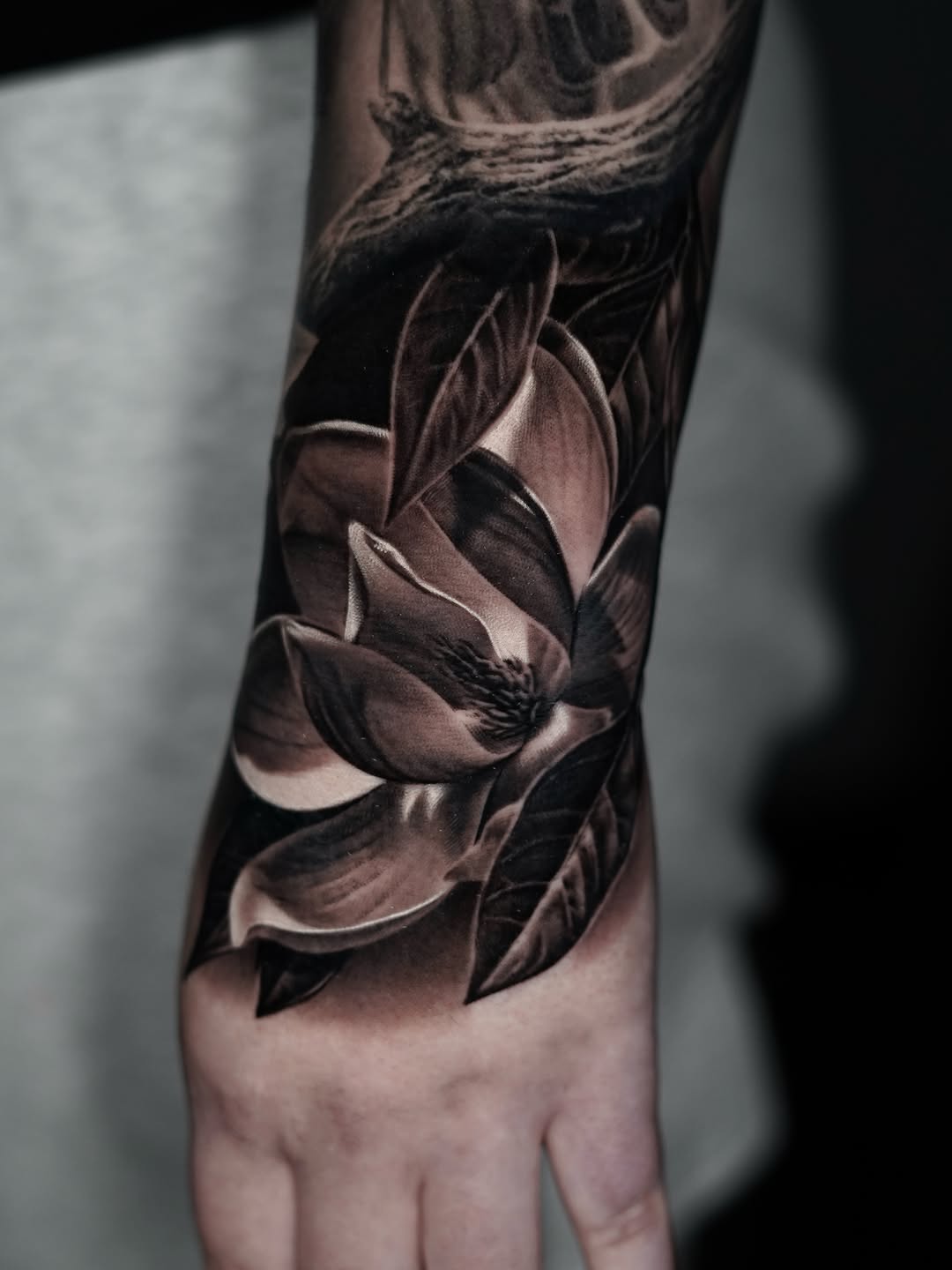 Photorealistic black and grey lotus flower with detailed petals and leaves on the hand and forearm.