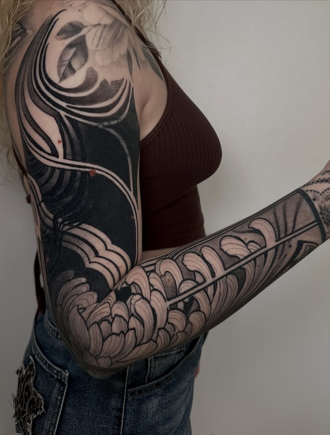 Full sleeve tattoo featuring organic flowing lines and floral patterns in black and grey shading on upper arm and forearm.