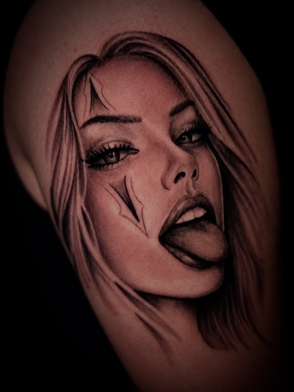 Black and grey portrait tattoo of a woman's face with long hair and dramatic shading on the upper arm.