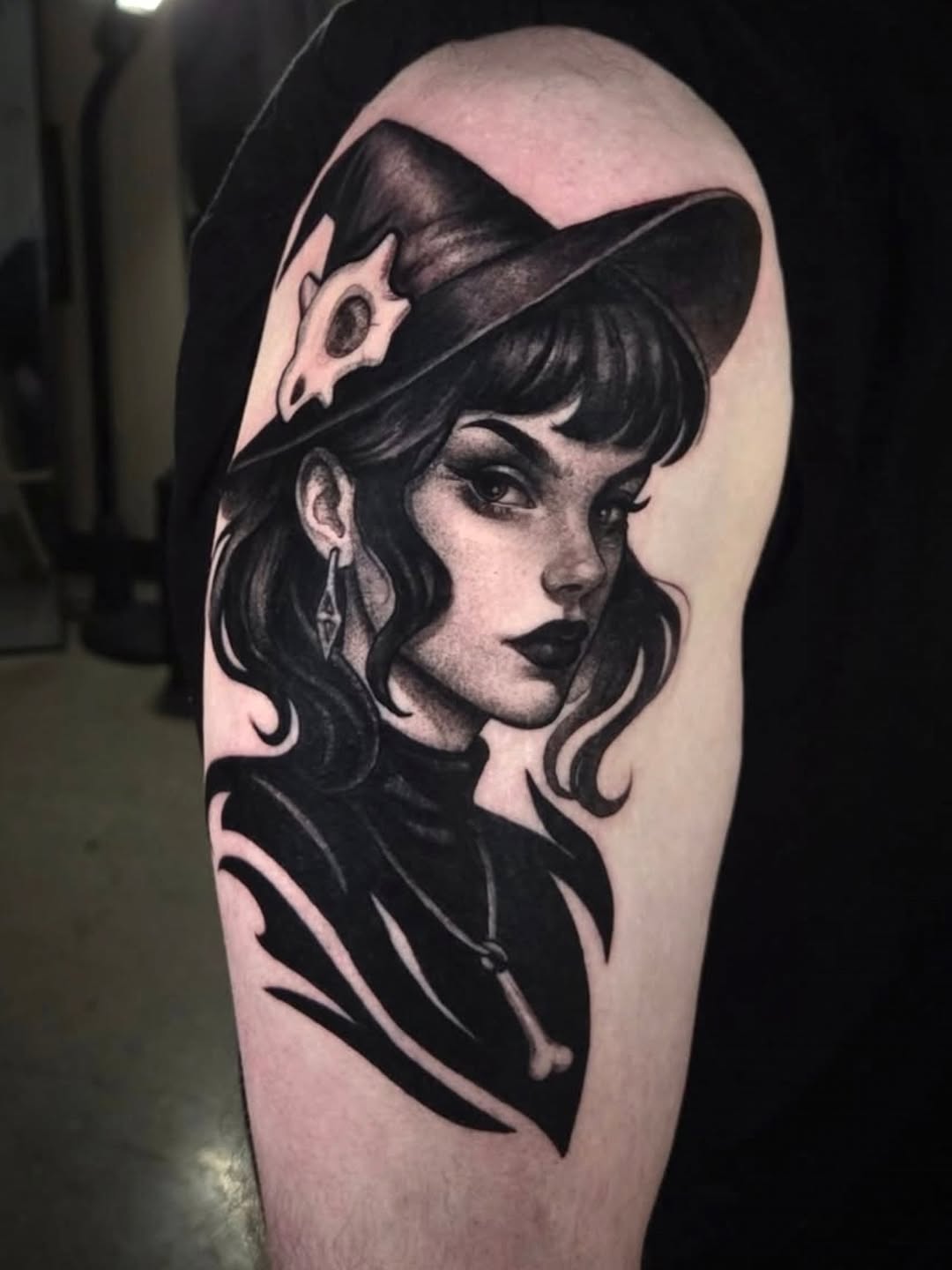 Black and grey portrait tattoo of a woman with wavy hair and fedora hat on upper arm, featuring smooth realistic shading.