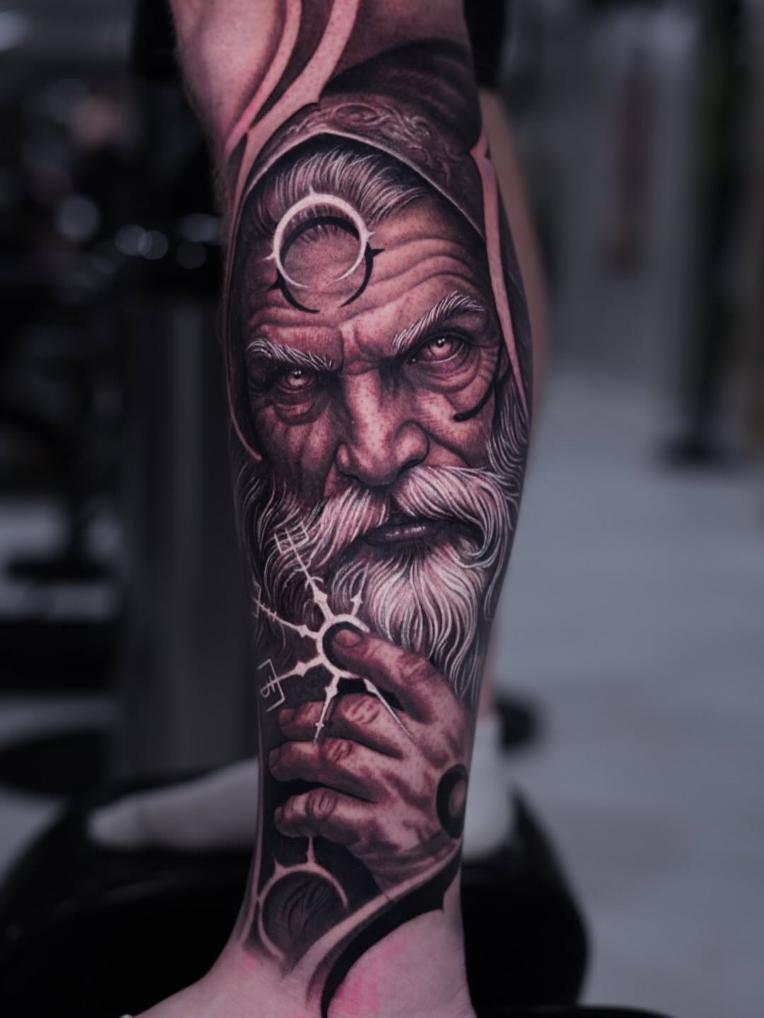 Detailed portrait of an elderly bearded man with circular symbols on forearm, rendered in black and grey shading on the arm.
