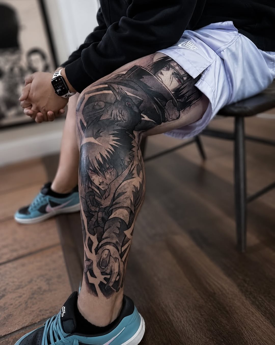 Black and grey leg sleeve tattoo featuring anime characters with detailed shading, displayed on seated person wearing light blue shorts.