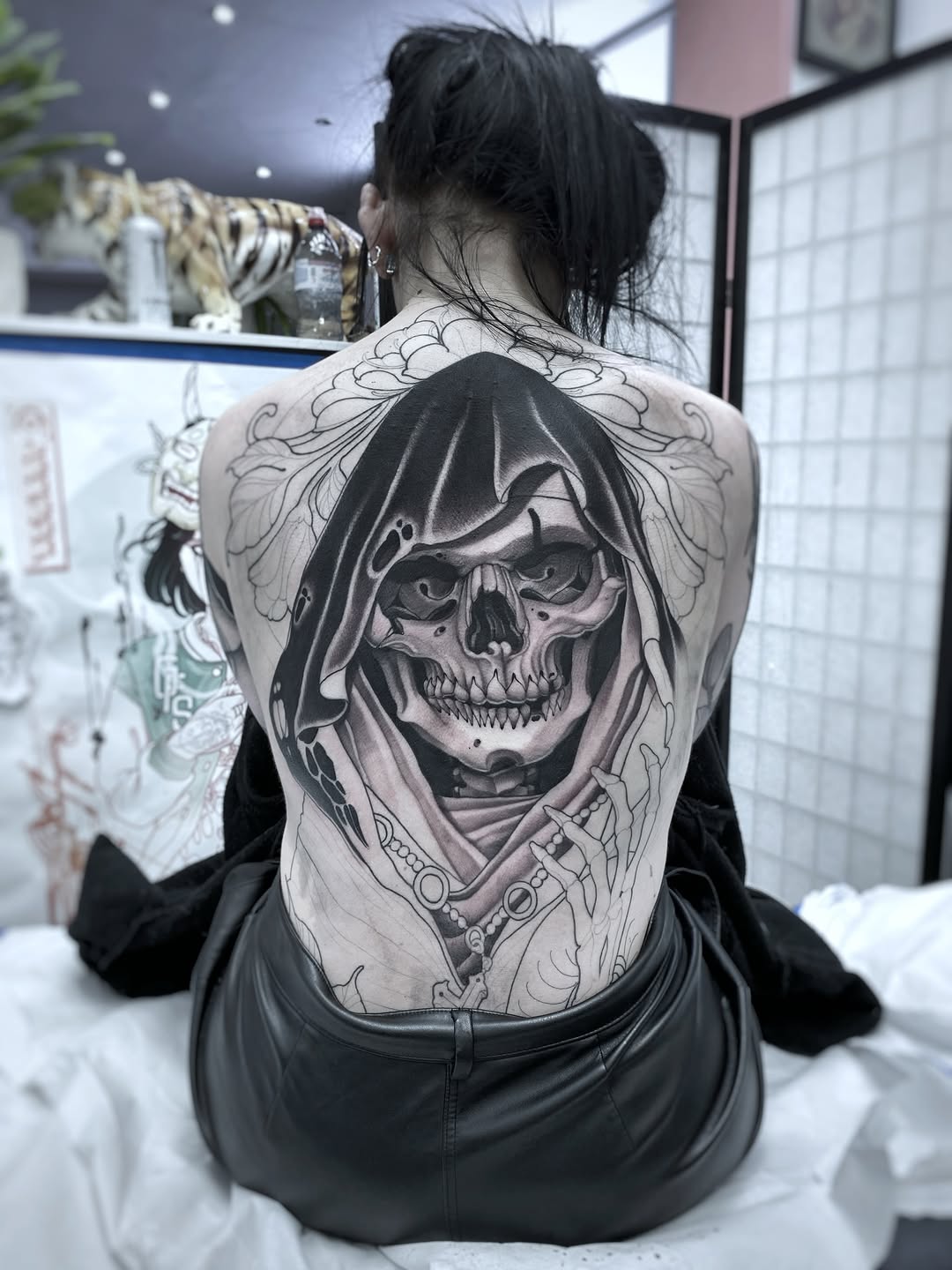 Grim reaper skull with hooded cloak and ornate decorative elements covering entire upper back in black and grey shading.