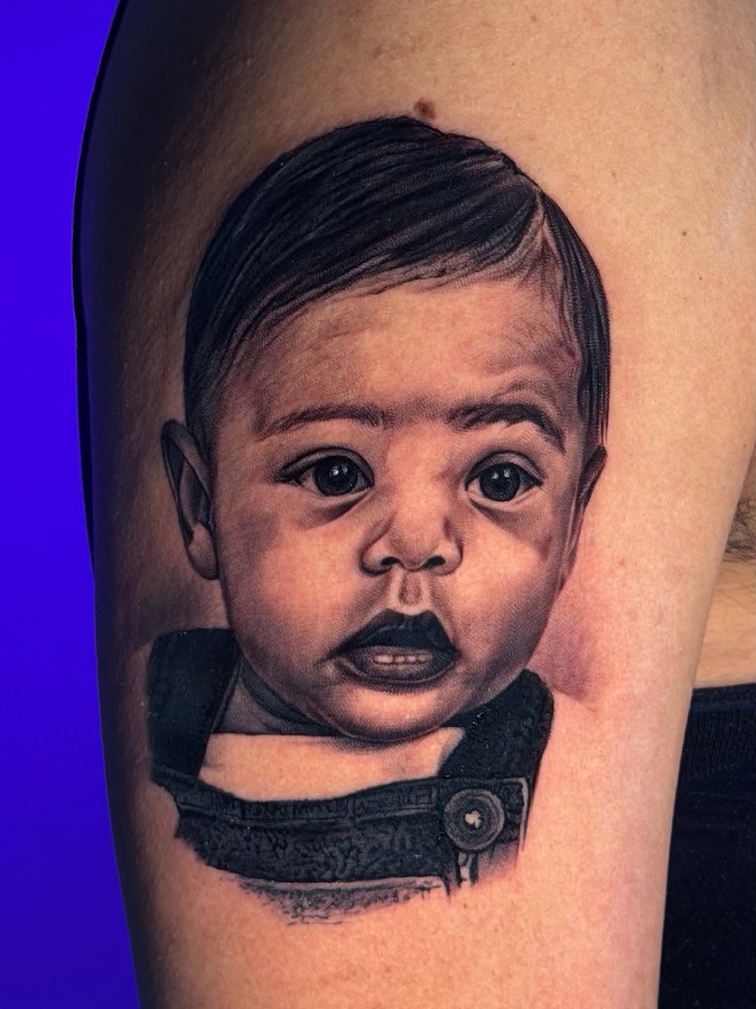 Baby's surprised face with dark hair and black clothing on upper arm, rendered in black and grey with smooth shading.