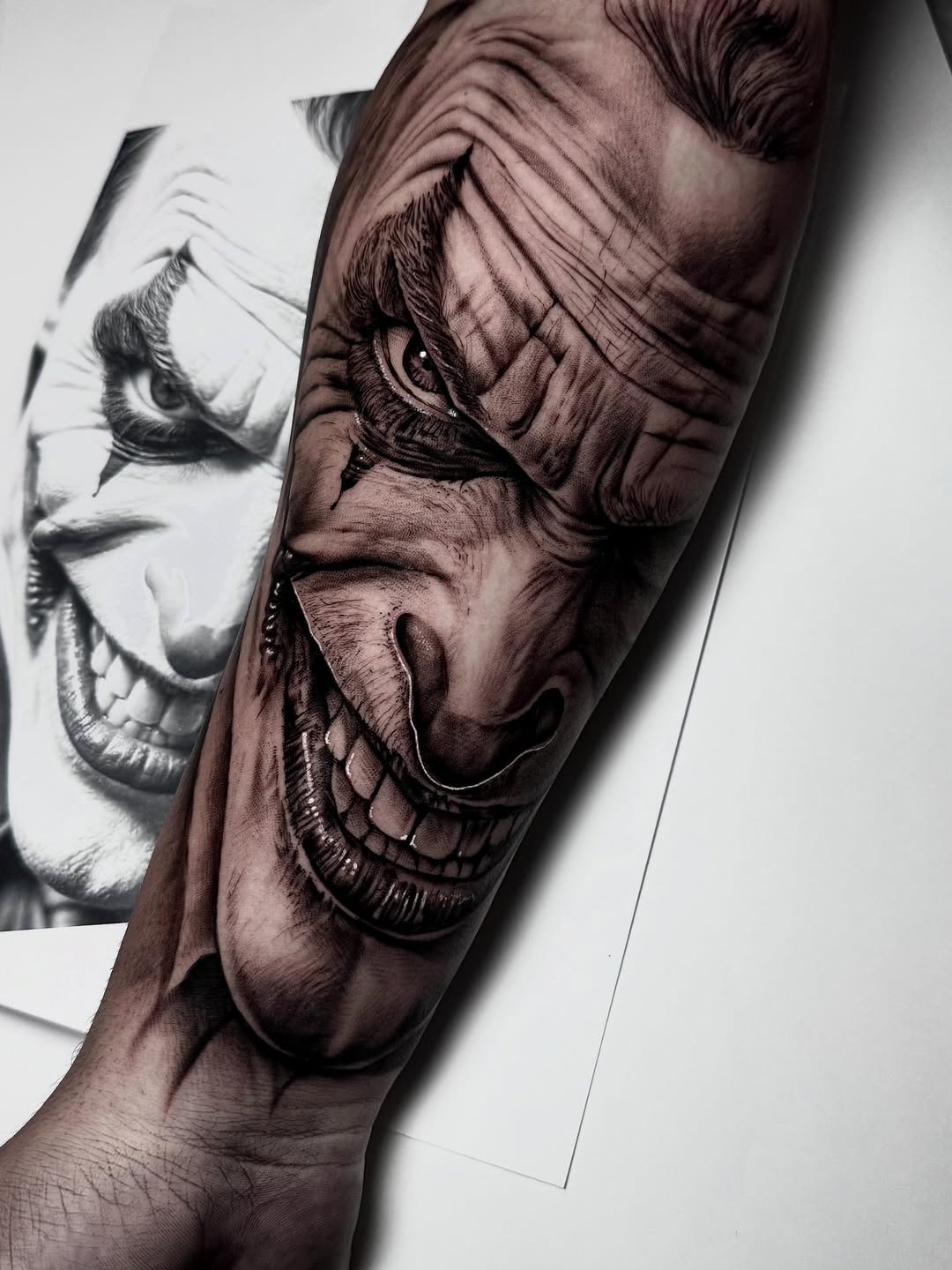 Detailed black and grey portrait tattoo on upper arm showing a face with skeletal features and intense expression with smooth shading.
