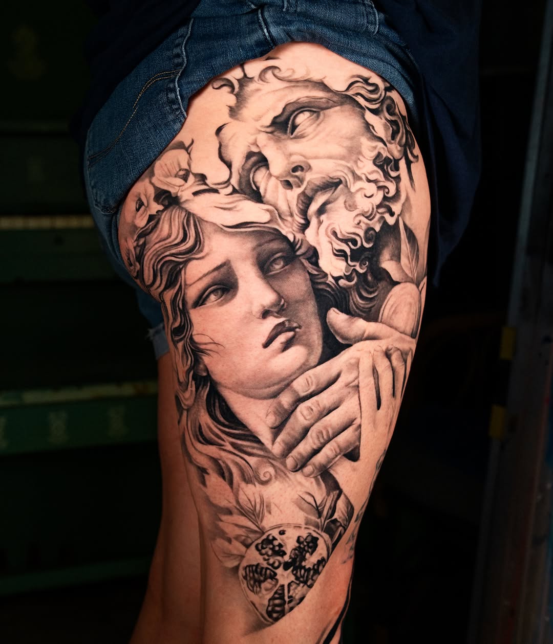 Monochromatic portrait tattoo of classical sculpted faces with curled hair and detailed facial features on thigh.