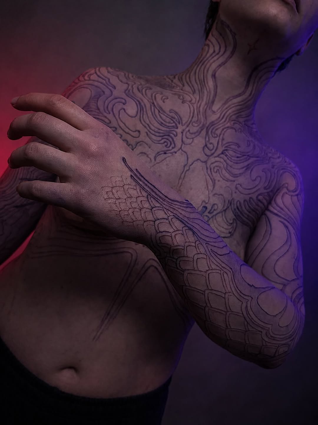 Ornate black and grey tattoo covering upper back and shoulder with flowing baroque-inspired patterns and scaled wing designs.