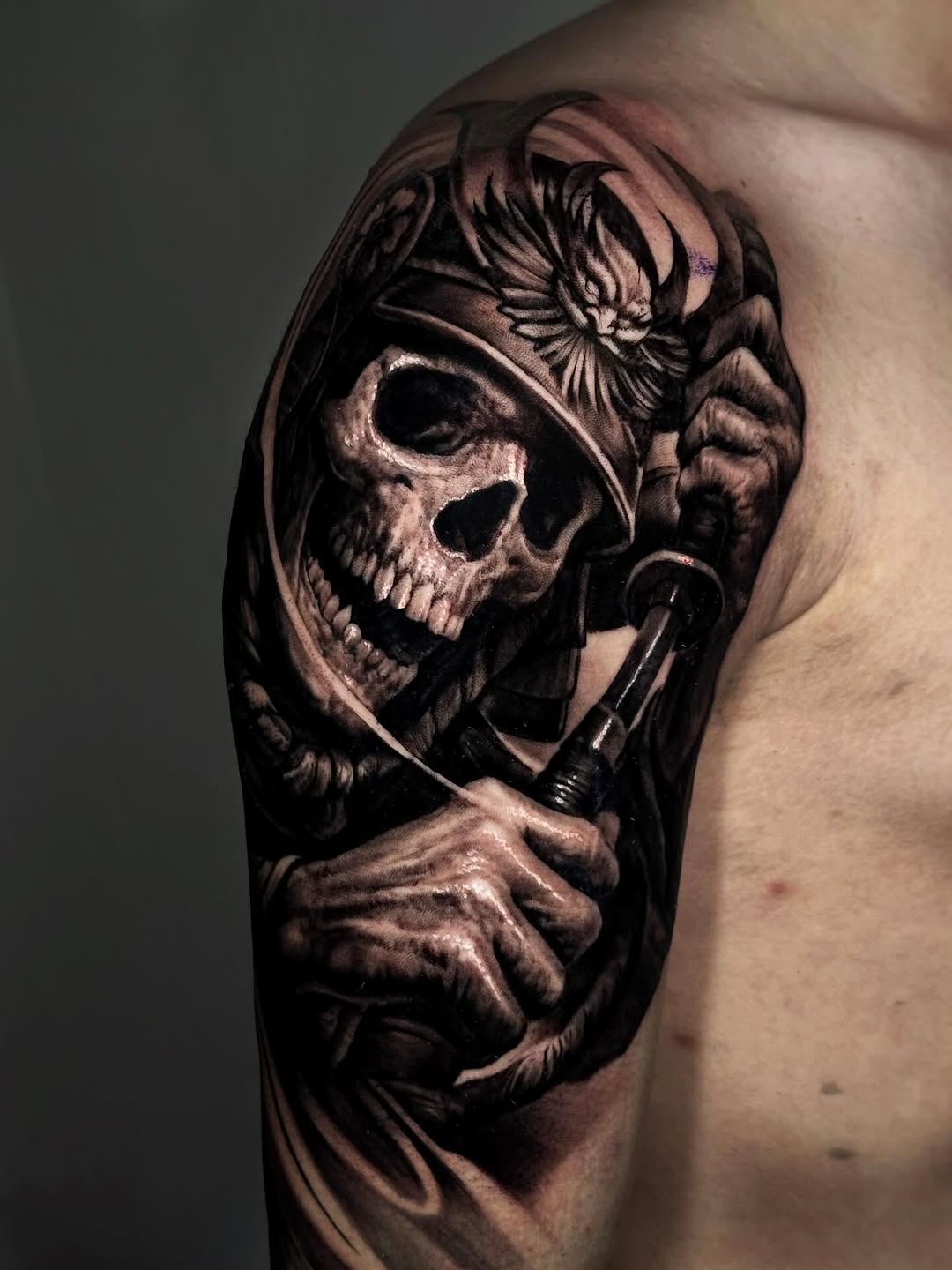 Black and grey shoulder tattoo of a skeletal soldier wearing a helmet, gripping rope and a knife, with a bird overhead.