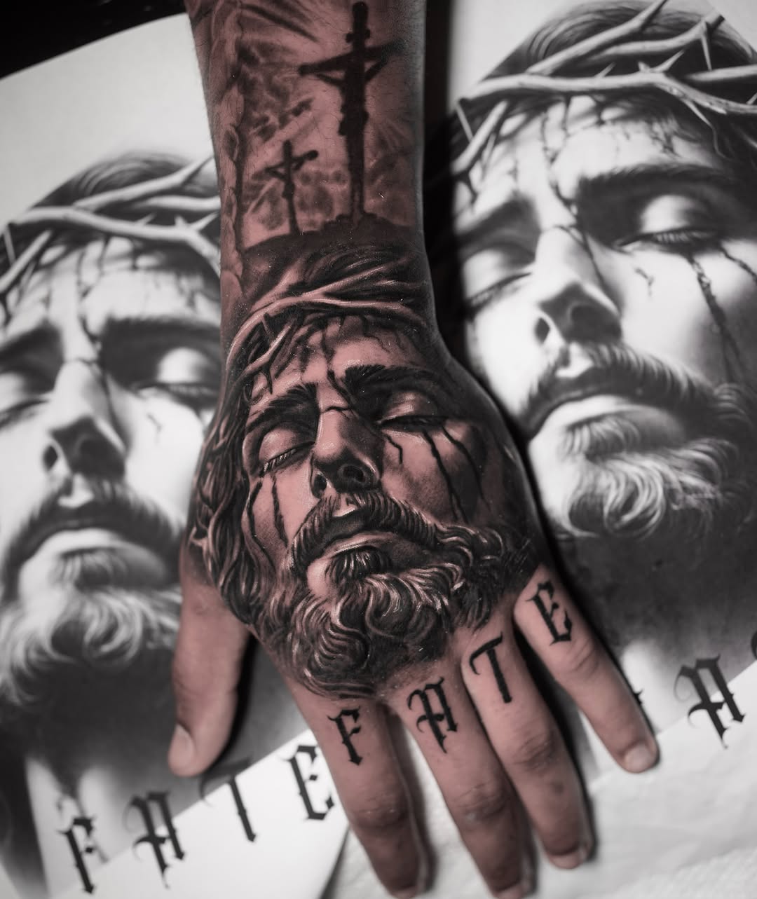 Hand tattoo featuring a detailed bearded male face with crown of thorns and cross, rendered in black and grey with smooth shading gradients.