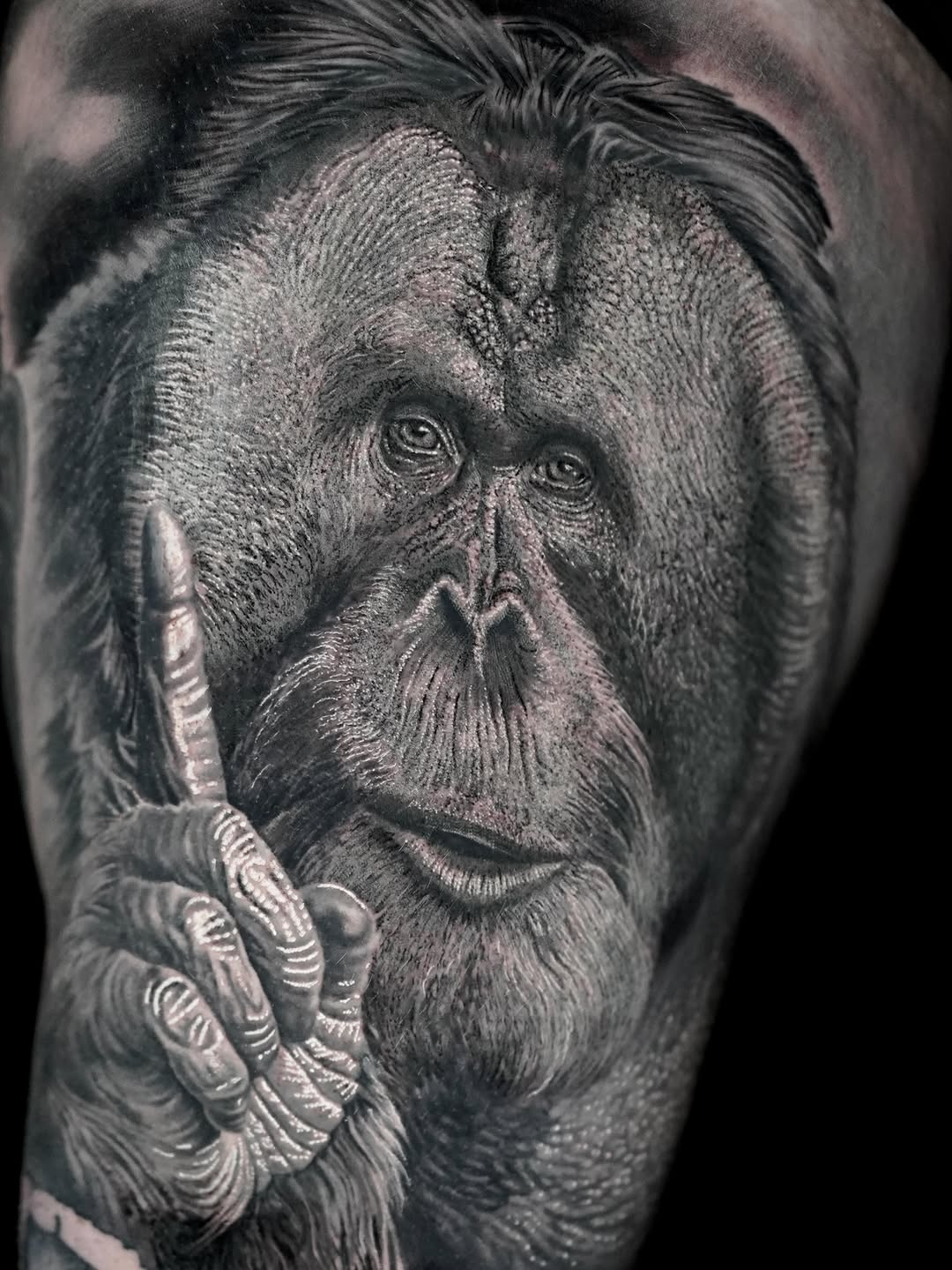 Photorealistic portrait of an orangutan's face with detailed fur texture and expressive eyes, rendered in black and grey on upper arm.