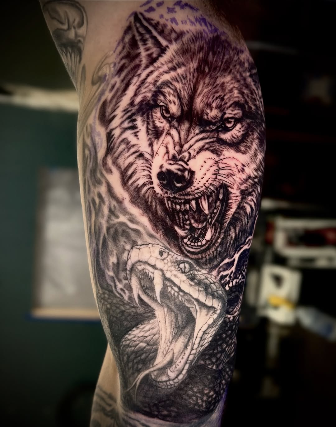 Aggressive snarling wolf head with detailed fur texture and open mouth showing teeth, tattooed on upper arm in black and grey shading.