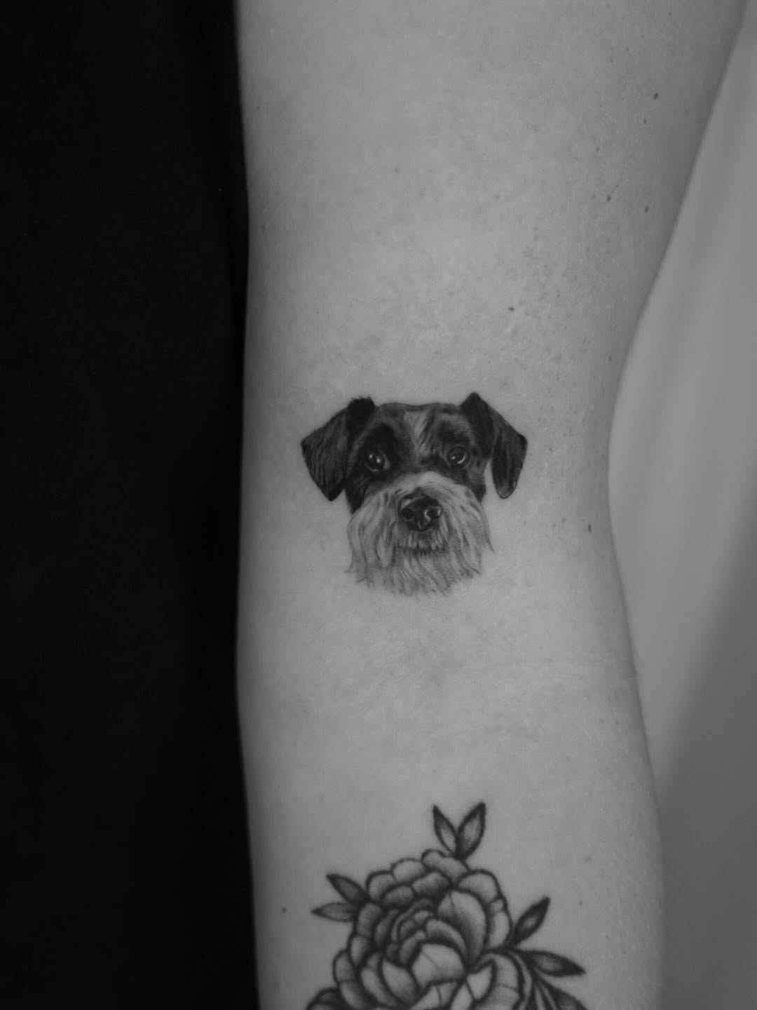 Black and grey portrait of a bearded dog's face on the leg, with a peony flower below.