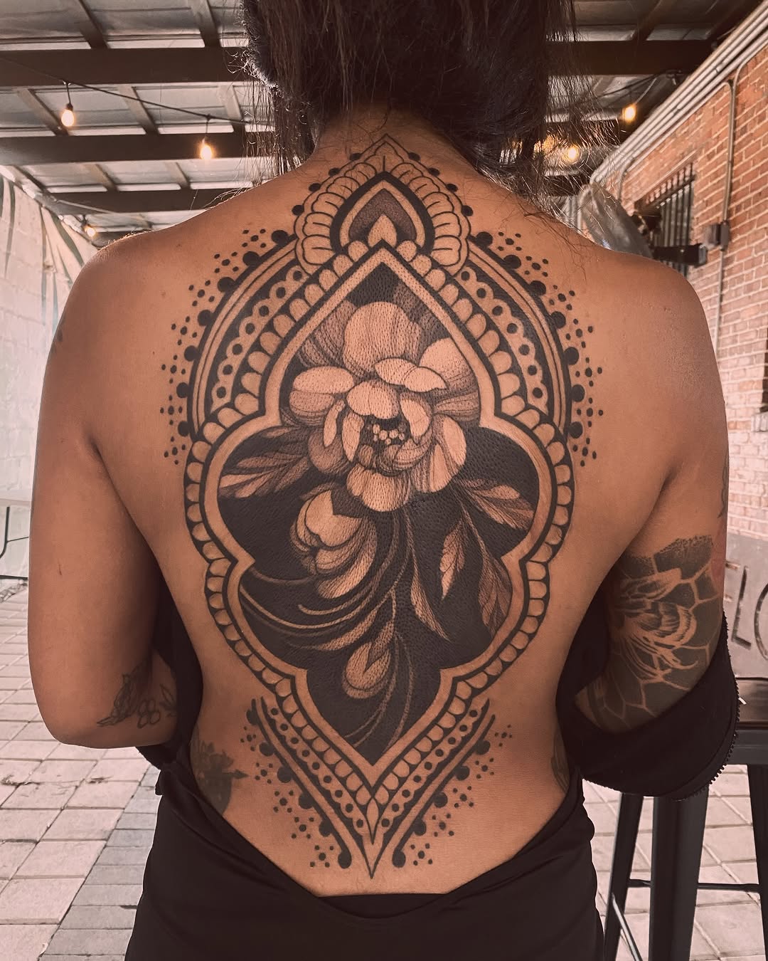 Back tattoo featuring a ornate mandala frame with a detailed peony flower in black and grey shading.
