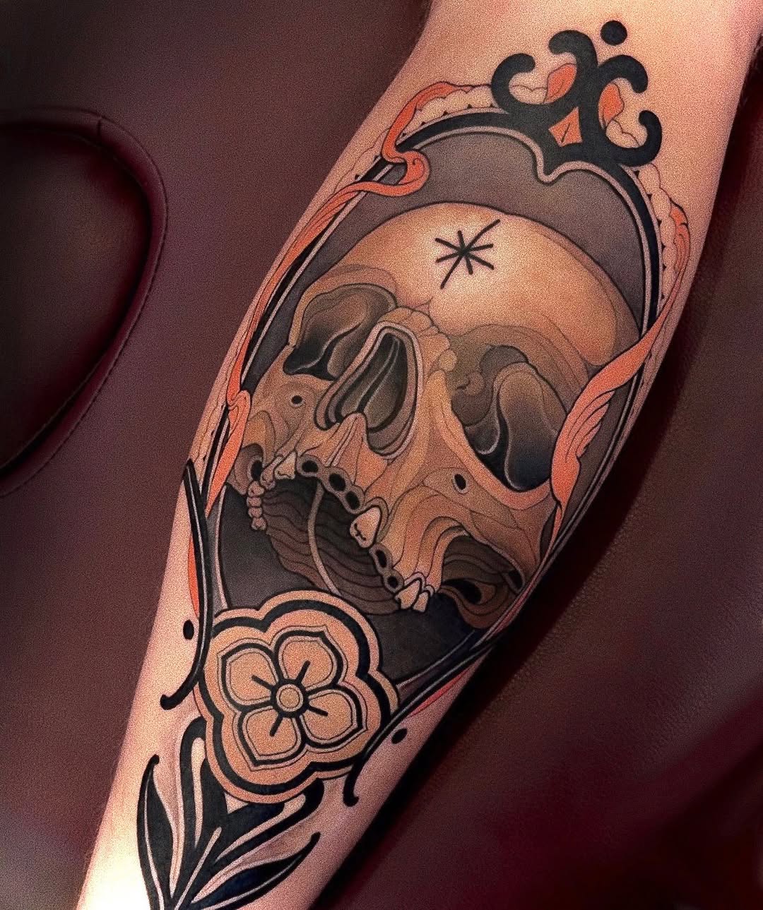 Skull with ornamental frame and flowers on forearm, rendered in black and grey with smooth shading gradients.