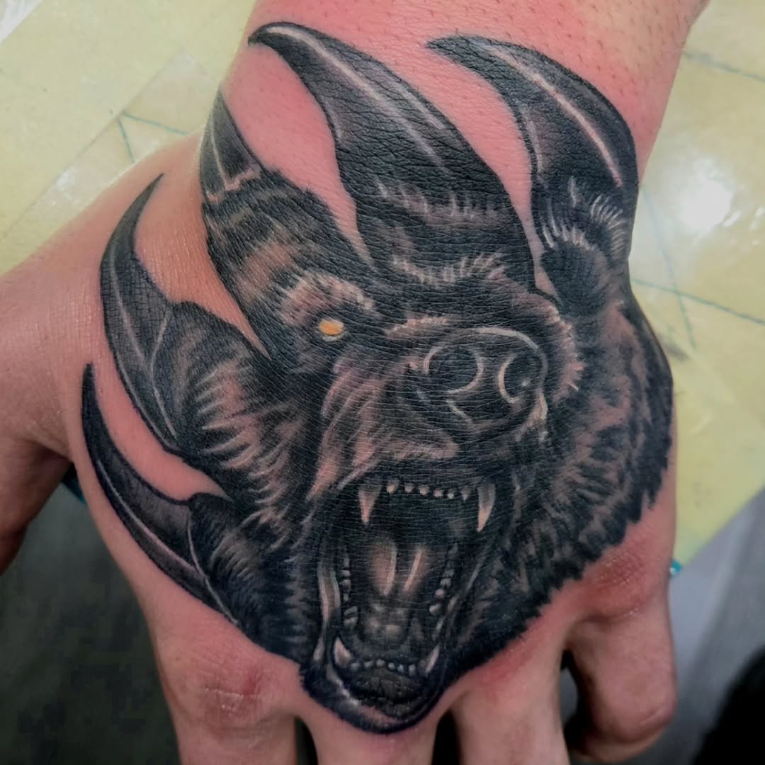 Black and grey demonic horned creature head with menacing expression and visible fangs tattooed on the back of a hand.
