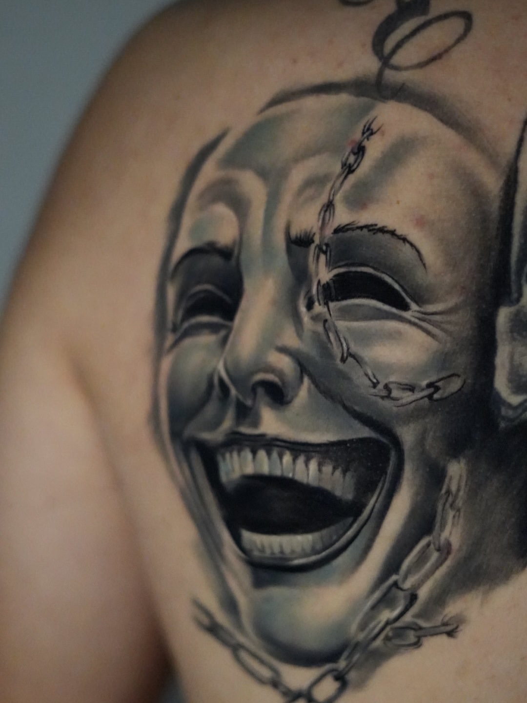 Two theatrical drama masks with stitched mouths in black and grey shading on upper arm, displaying detailed realism with smooth gradients.