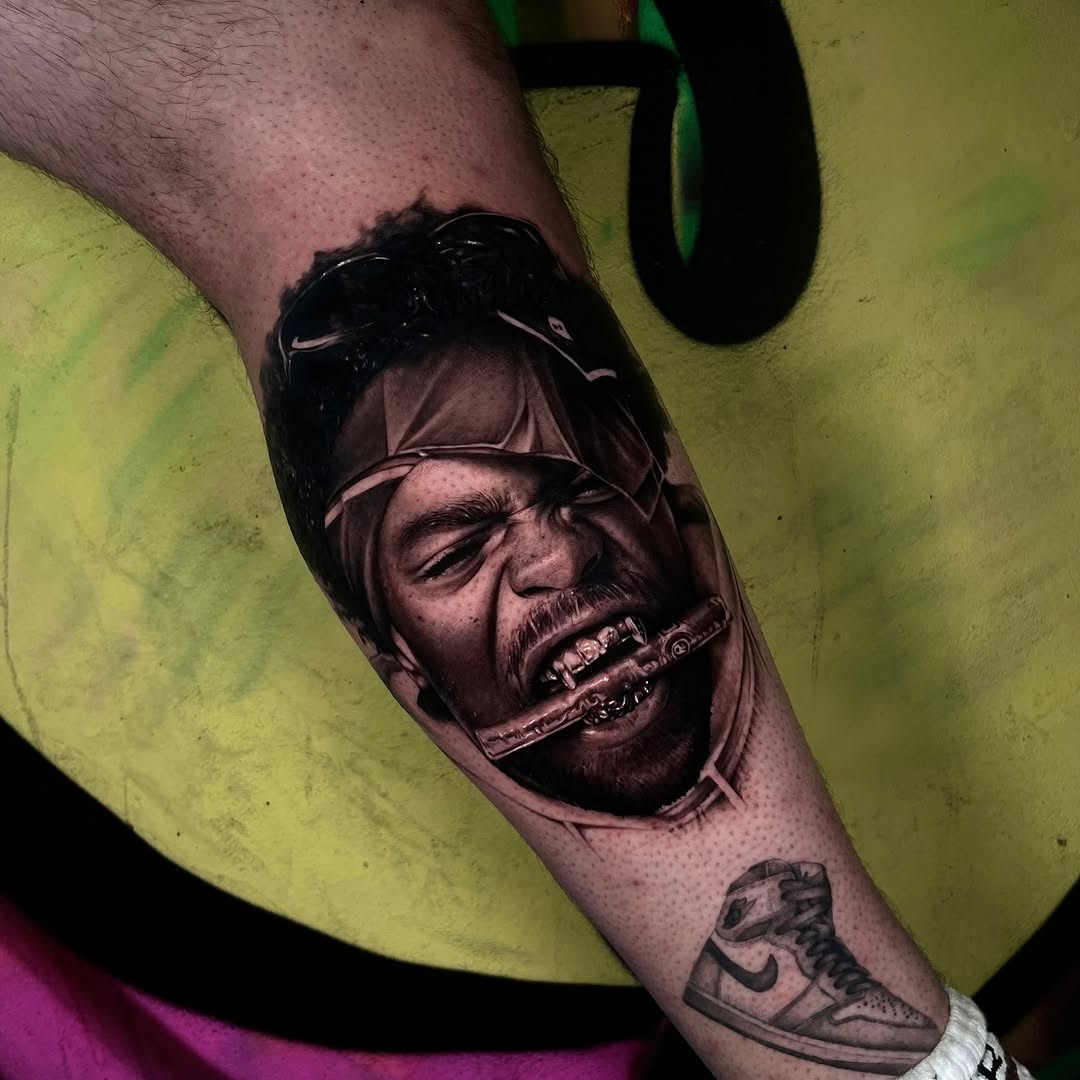 Portrait tattoo of a man wearing sunglasses with a cigar, rendered in black and grey with soft shading on the forearm.