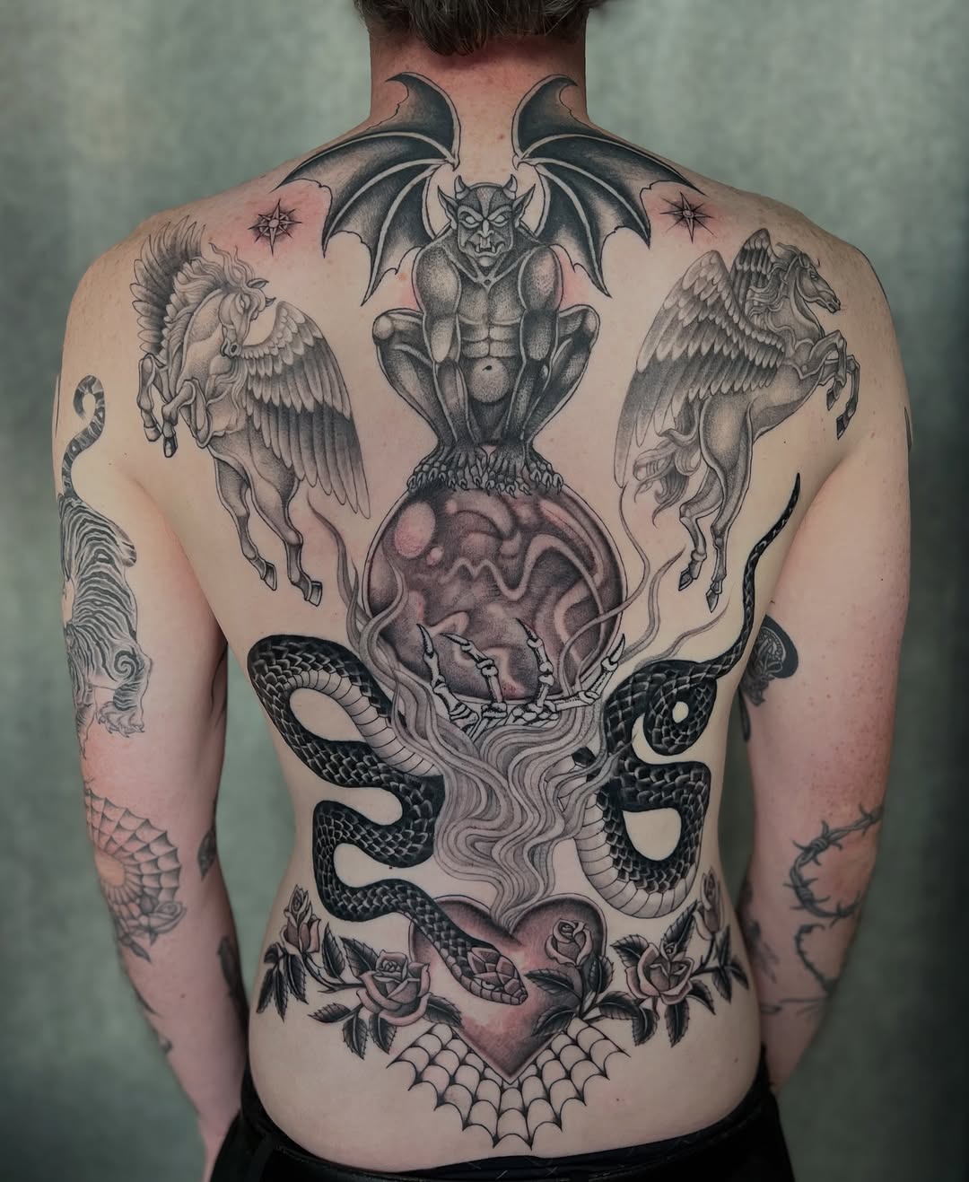 Back piece featuring a demon perched on a heart with intertwined snakes, flanked by winged creatures, rendered in black and grey.