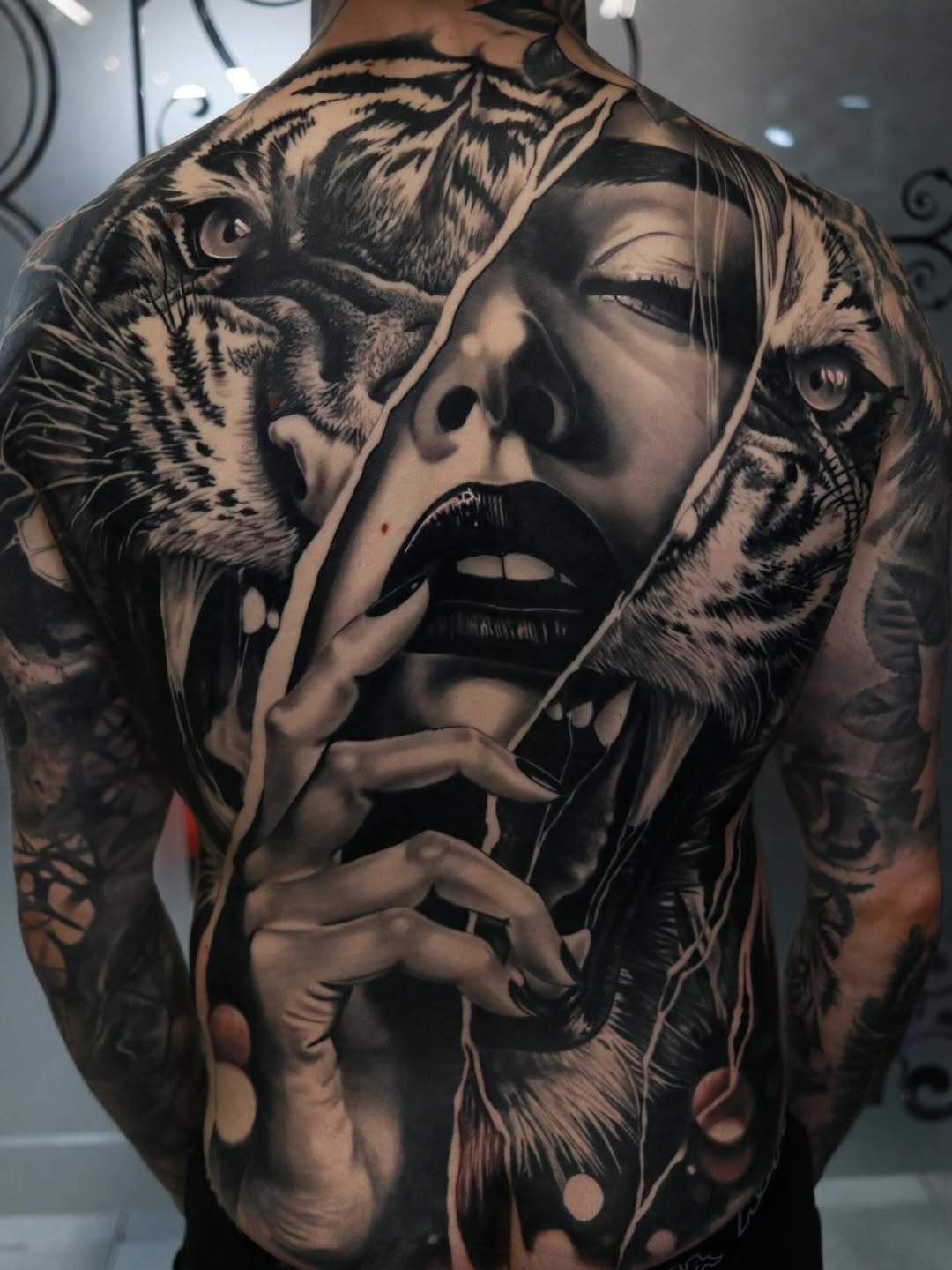 Back tattoo featuring a woman's face with tigers flanking either side, rendered in black and grey with smooth shading and realistic detail.