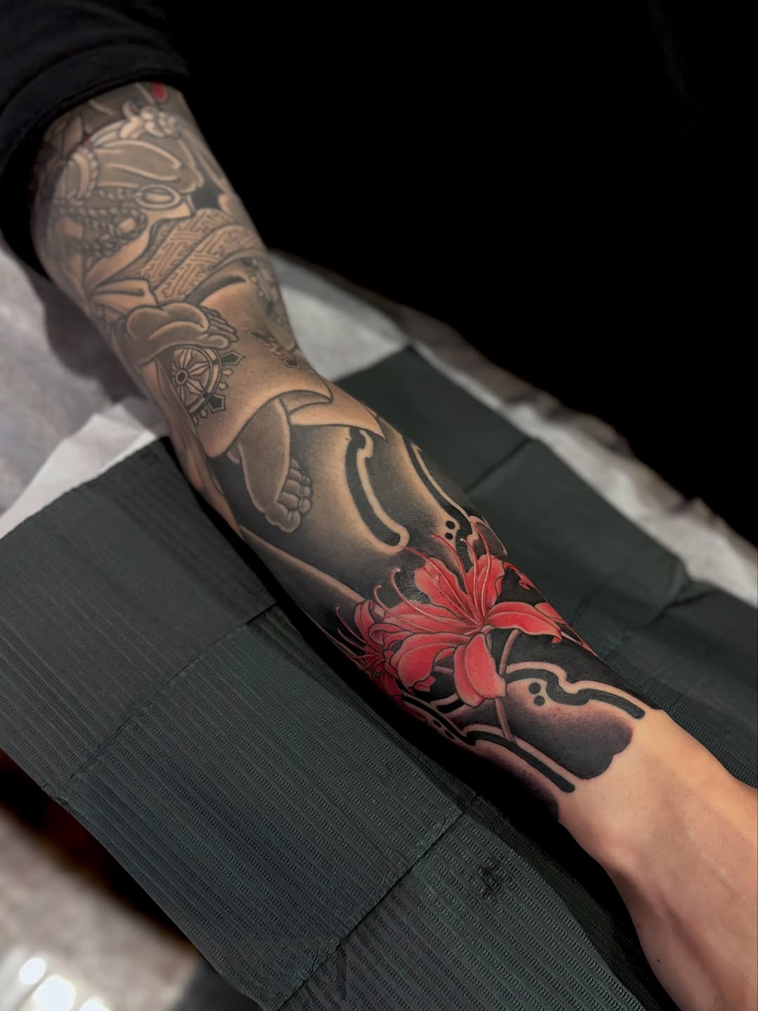 Full forearm sleeve tattoo featuring ornate designs, a red flower centerpiece, and decorative elements in black and grey shading on pale skin.