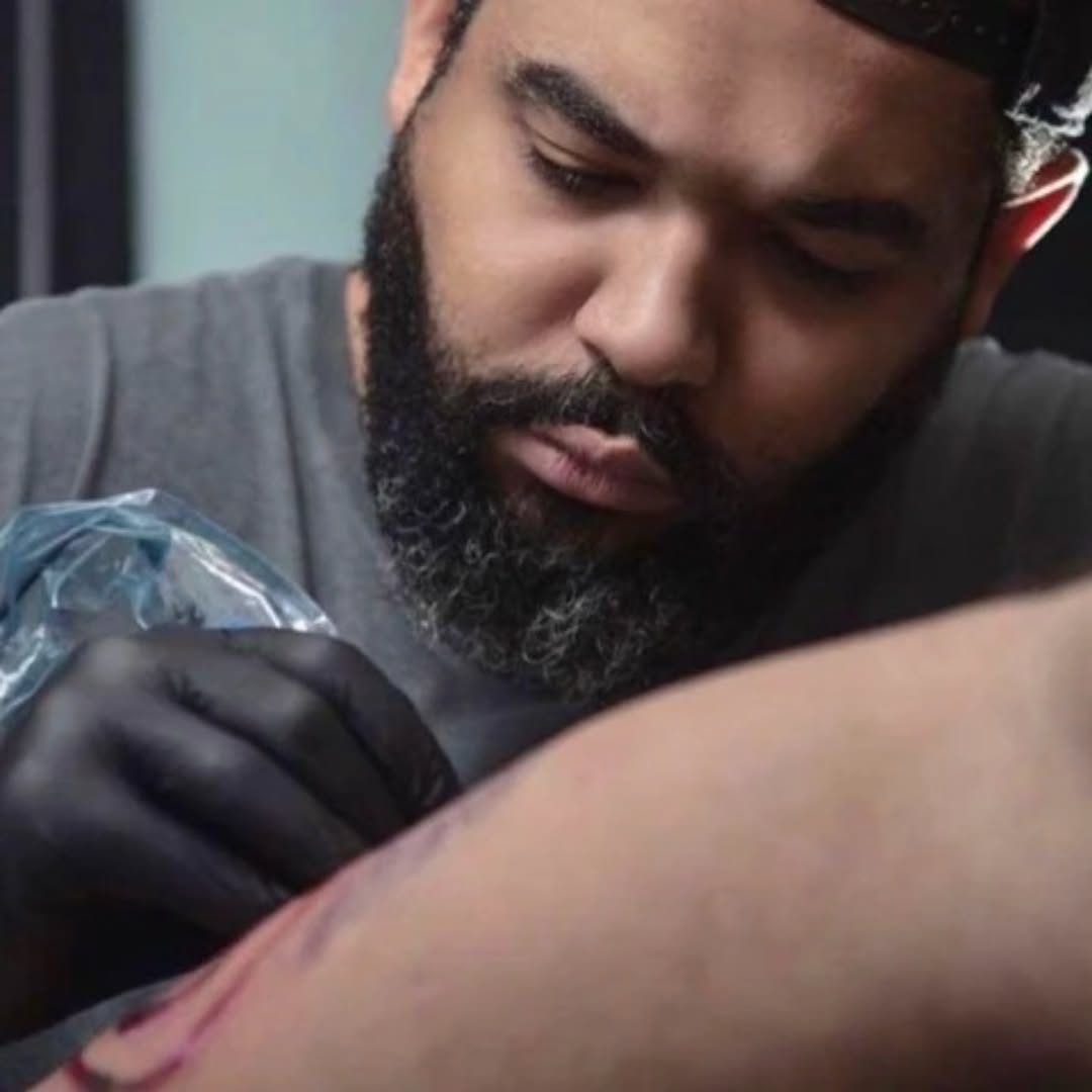 Black and grey realistic tattoo on upper arm featuring detailed portrait with smooth shading and gradient tones.