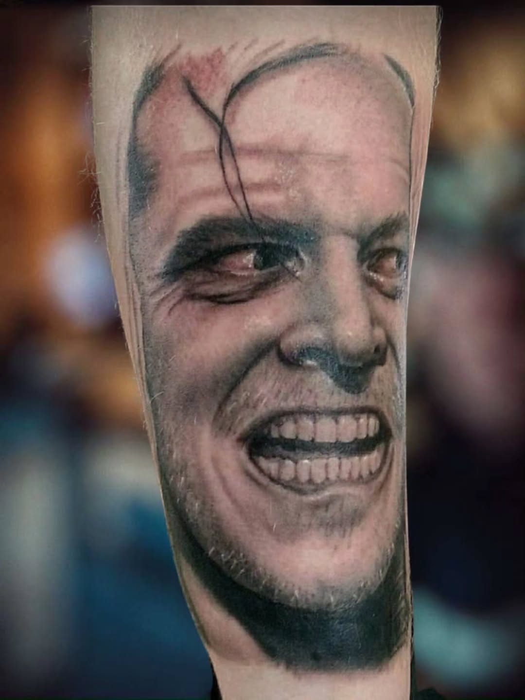 Realistic black and grey portrait tattoo of a man's face with intense expression on forearm, showing detailed facial features and shading.