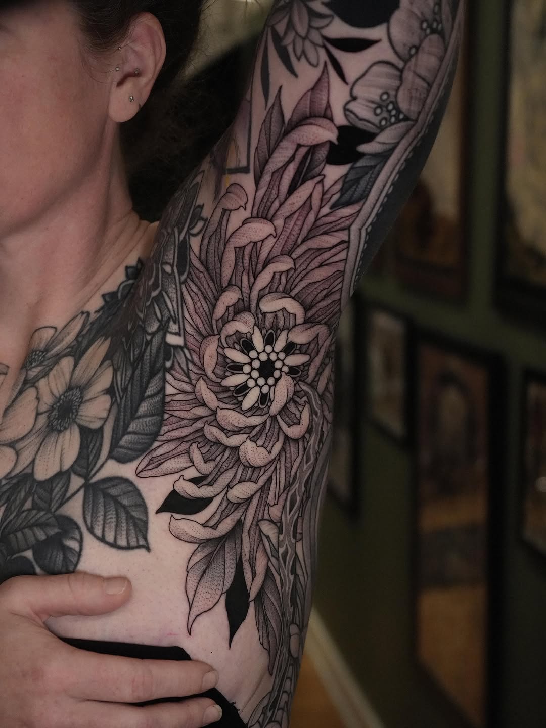Black and grey floral sleeve tattoo featuring detailed flowers with soft shading on a person's arm and chest area.