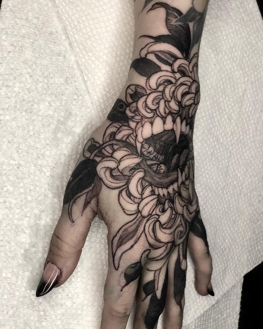 Black and grey floral sleeve tattoo featuring chrysanthemums and decorative botanical elements on forearm and hand with soft shading.