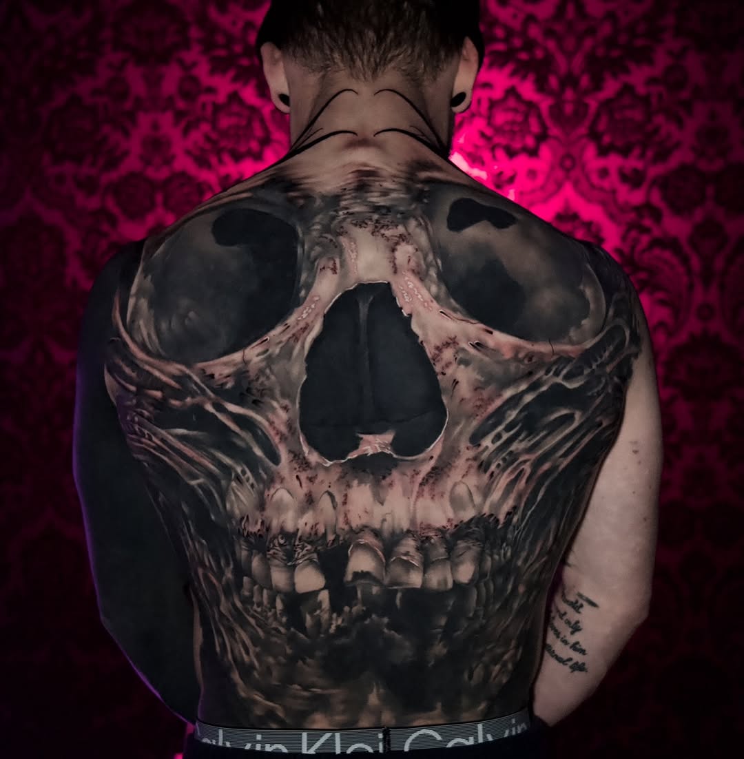 Large skull tattoo with detailed shading and texture covering the entire upper back, rendered in black and grey tones.
