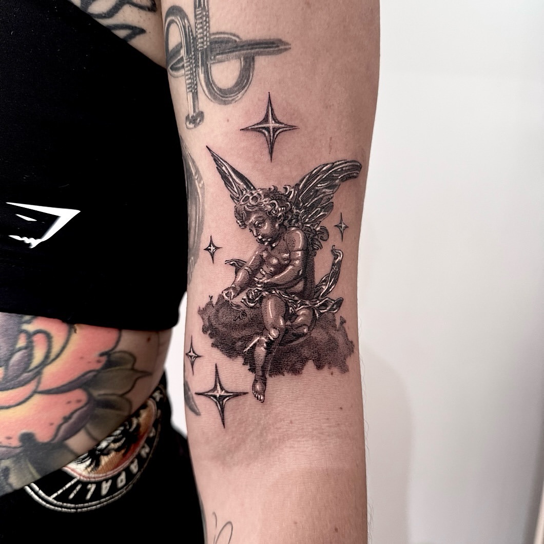Cherub angel sitting on clouds with wings, surrounded by four-pointed stars, rendered in black and grey on inner arm.