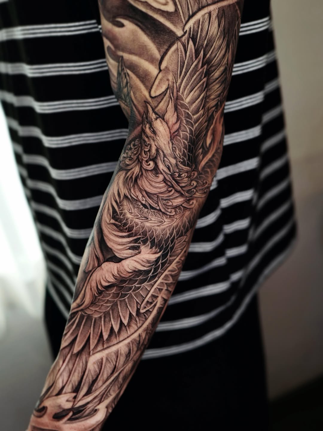 Detailed black and grey phoenix tattoo covering the full forearm with intricate feather work and shading on the upper arm.