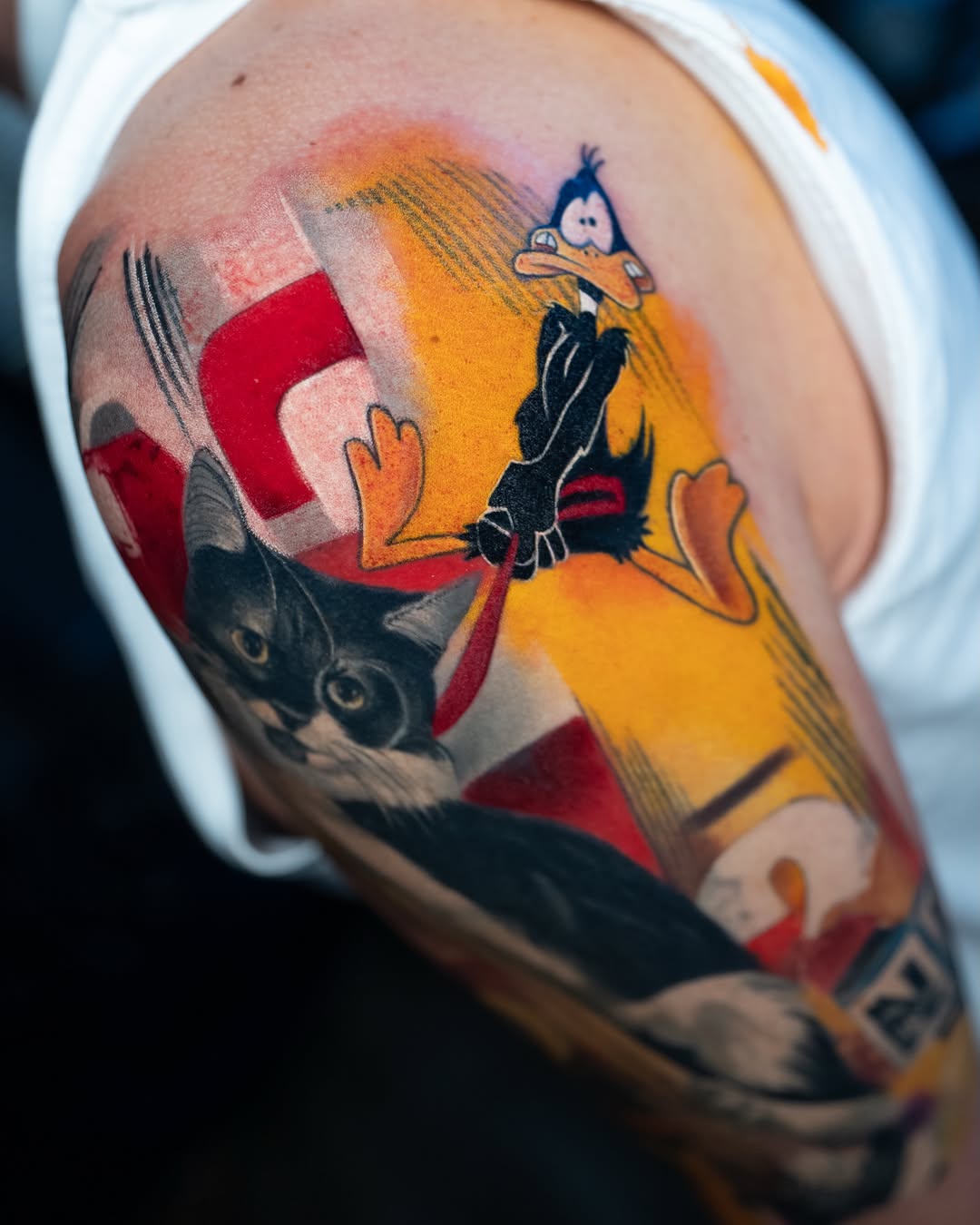 Cartoon bird character in yellow outfit with red geometric shapes and black cat face on upper arm.