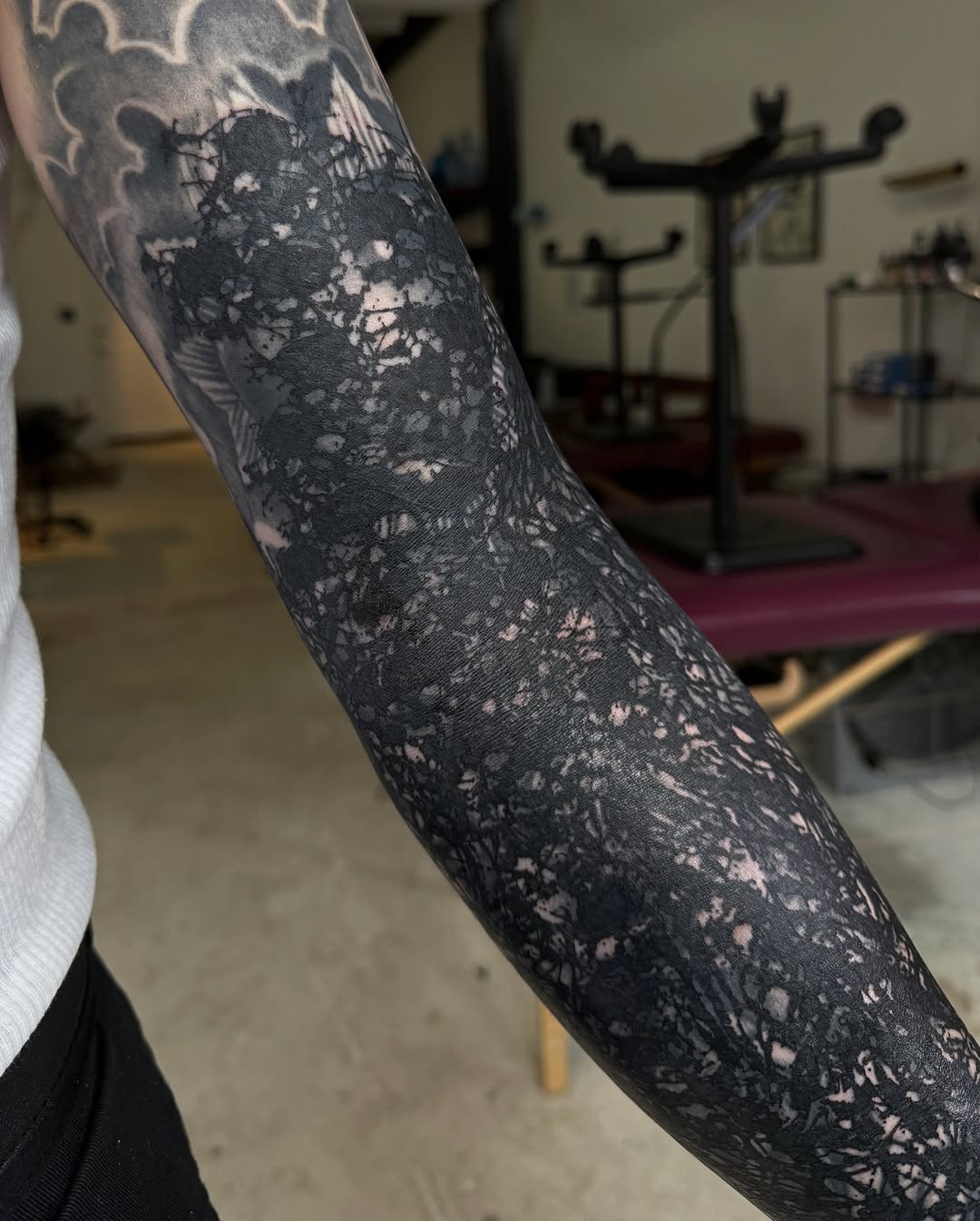 Black and grey monochromatic tattoo with textured splatter effects covering previous ink on the forearm.