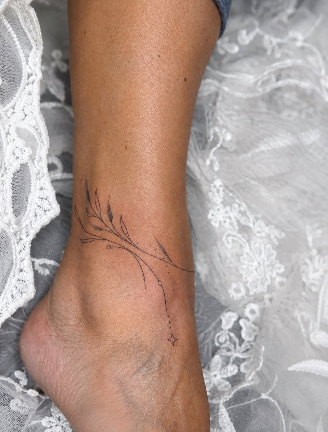 Delicate single-needle botanical branch with leaves and small stars on inner ankle, framed by white lace.