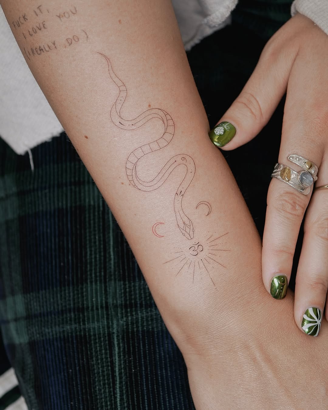 Delicate single-needle snake, moon, and sun symbols arranged vertically on the forearm with minimal shading.