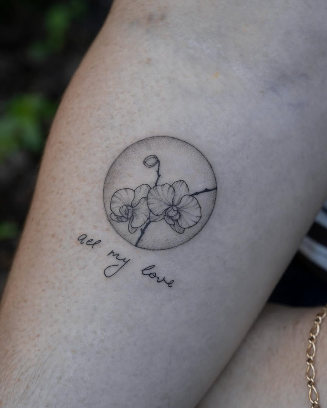 Delicate line-work orchid flowers in a circle with curling stem detail and script text below on forearm.
